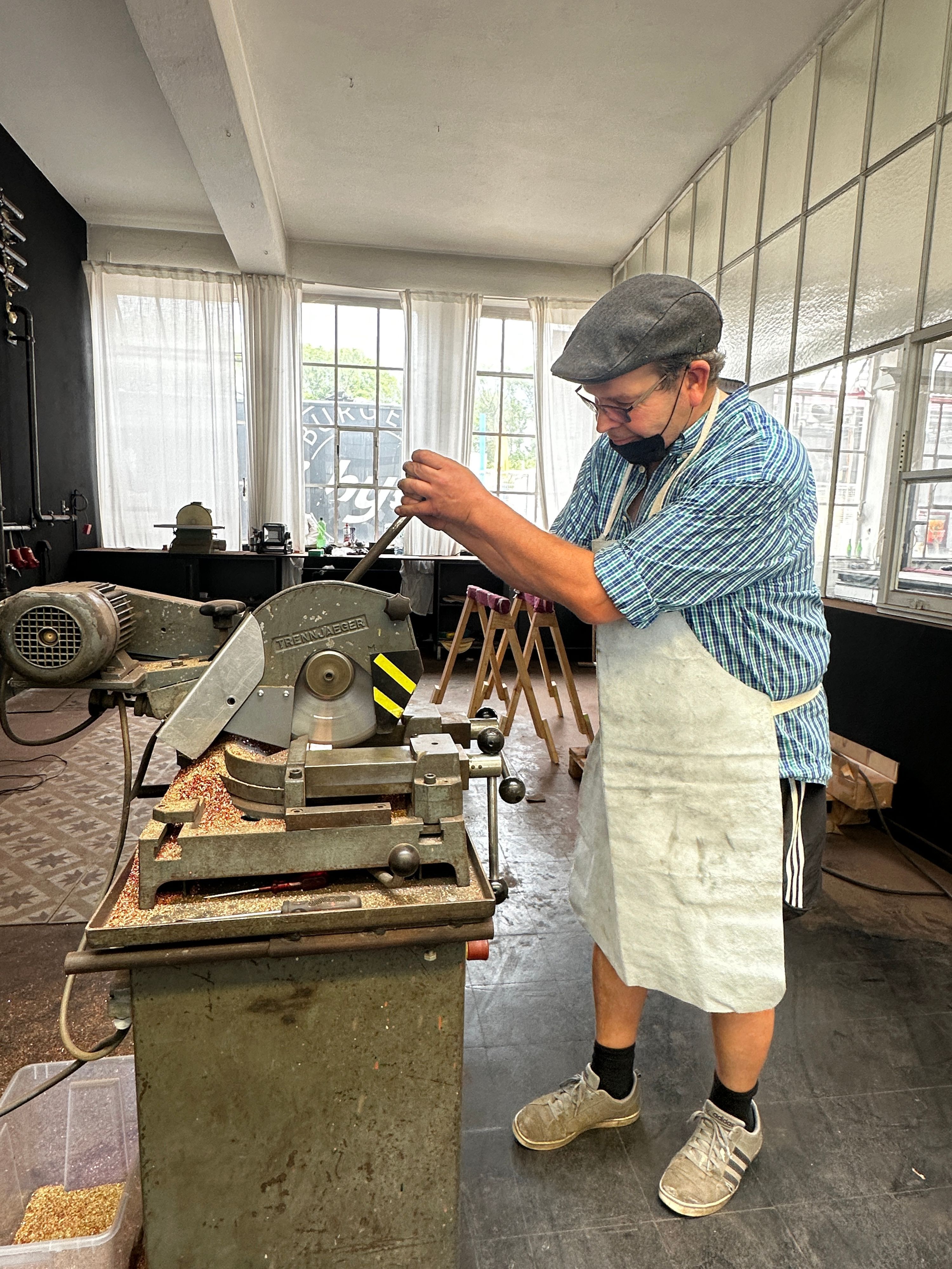Ein Mann im Arbeitskittel und mit Mundschutz steht an der Kuperschneide-Maschine.
