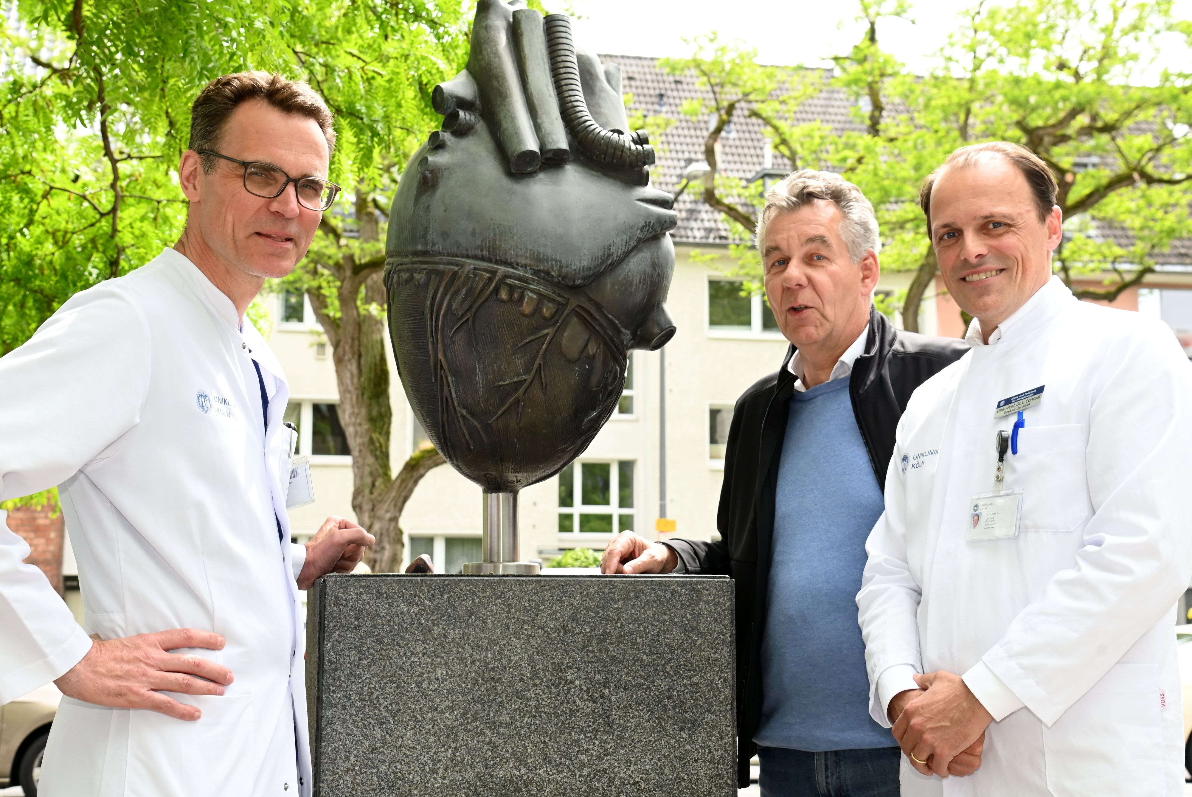 Peter Wessling (Mitte) vor der Kölner Uniklinik mit Herzskulptur und den Herzspezialisten Stephan Baldus (l.) und Lenard Conradi.