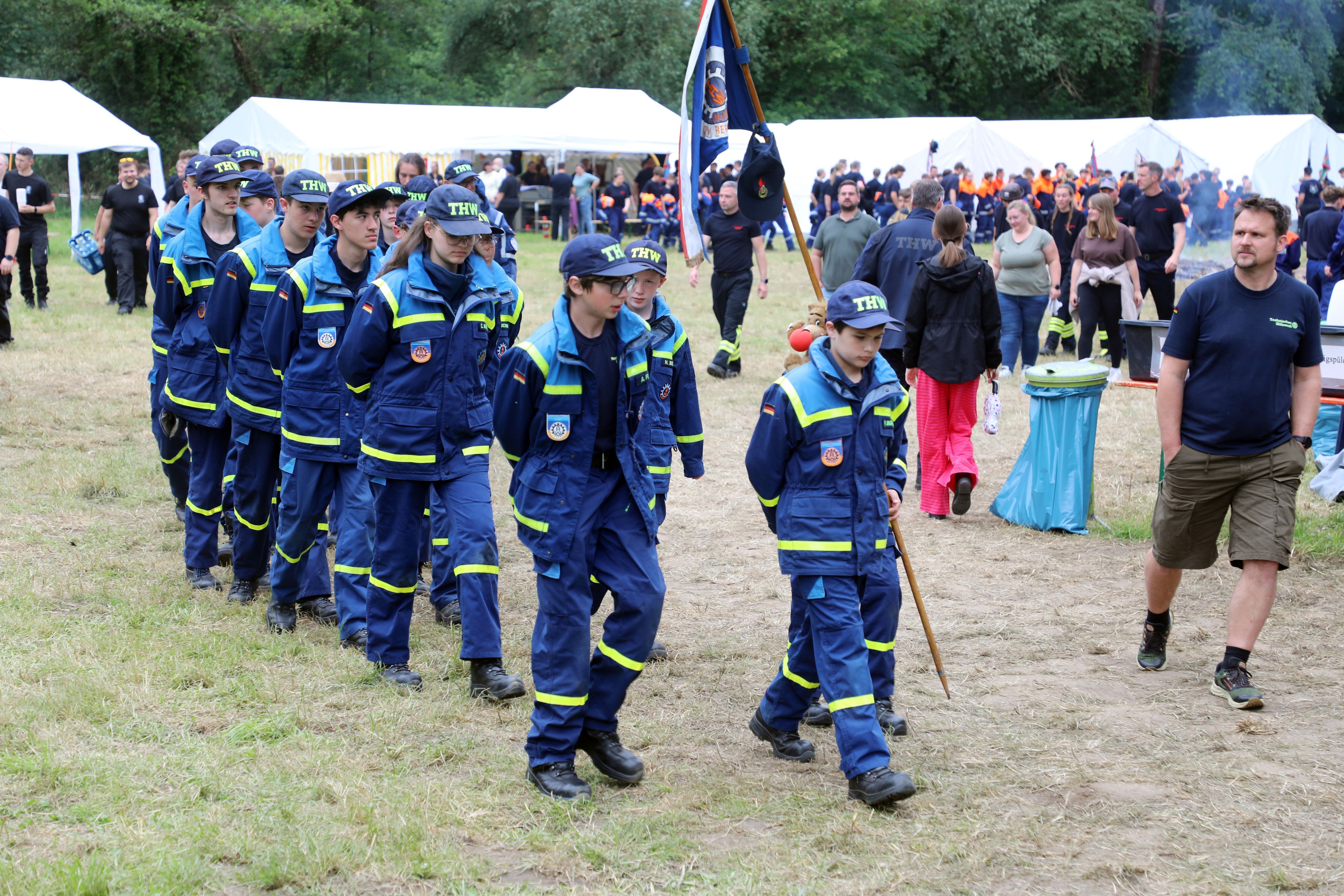 Eine THW-Jugendgruppe marschiert mit Wimpel über den Zeltplatz des Kreisjugendfeuerwehrzeltlagers 2026 in Bergisch Gladbach-Paffrath.