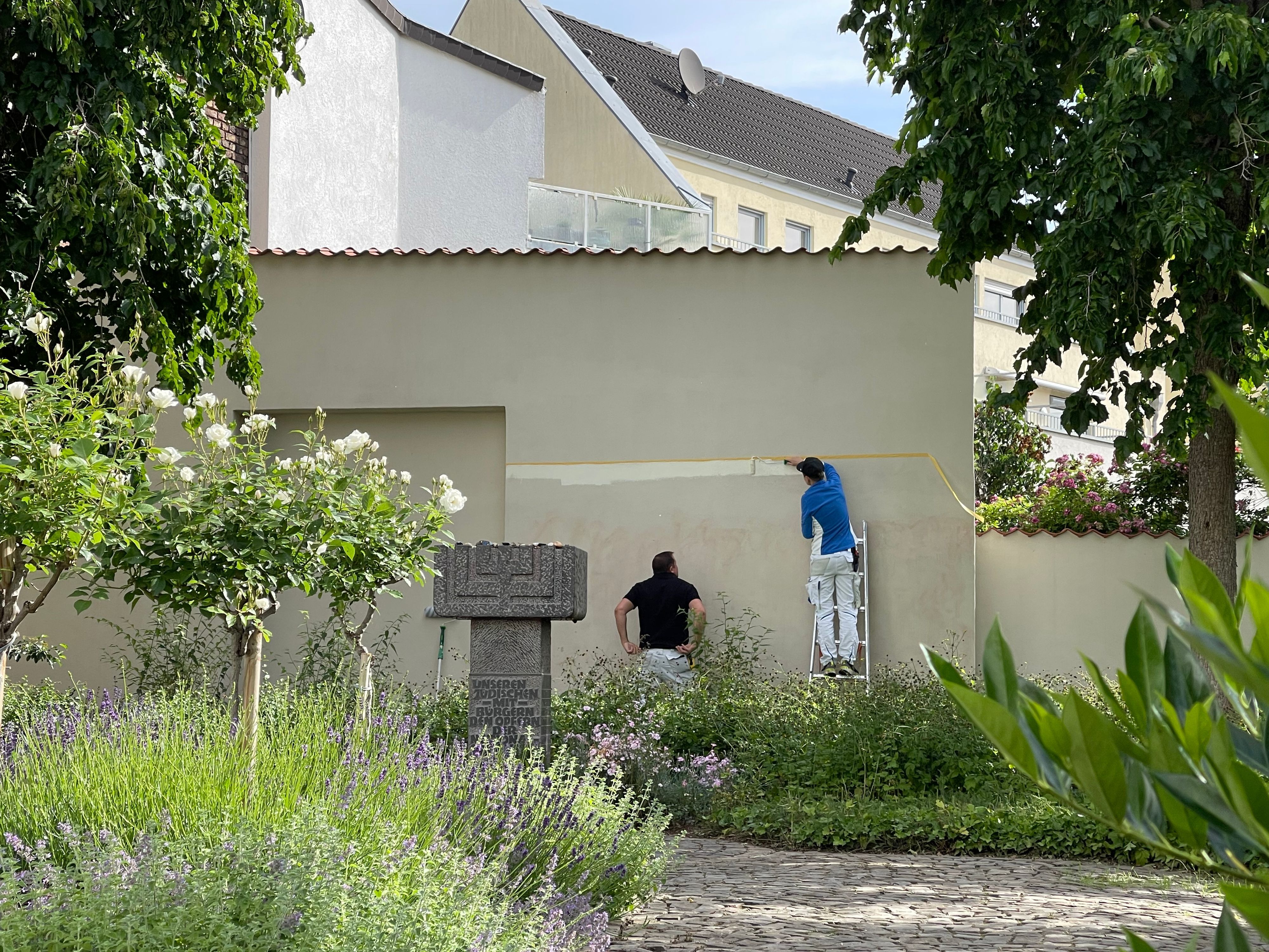 Ein Handwerker steht auf einer Leiter, seine Kollege sieht ihm bei der Arbeit zu.