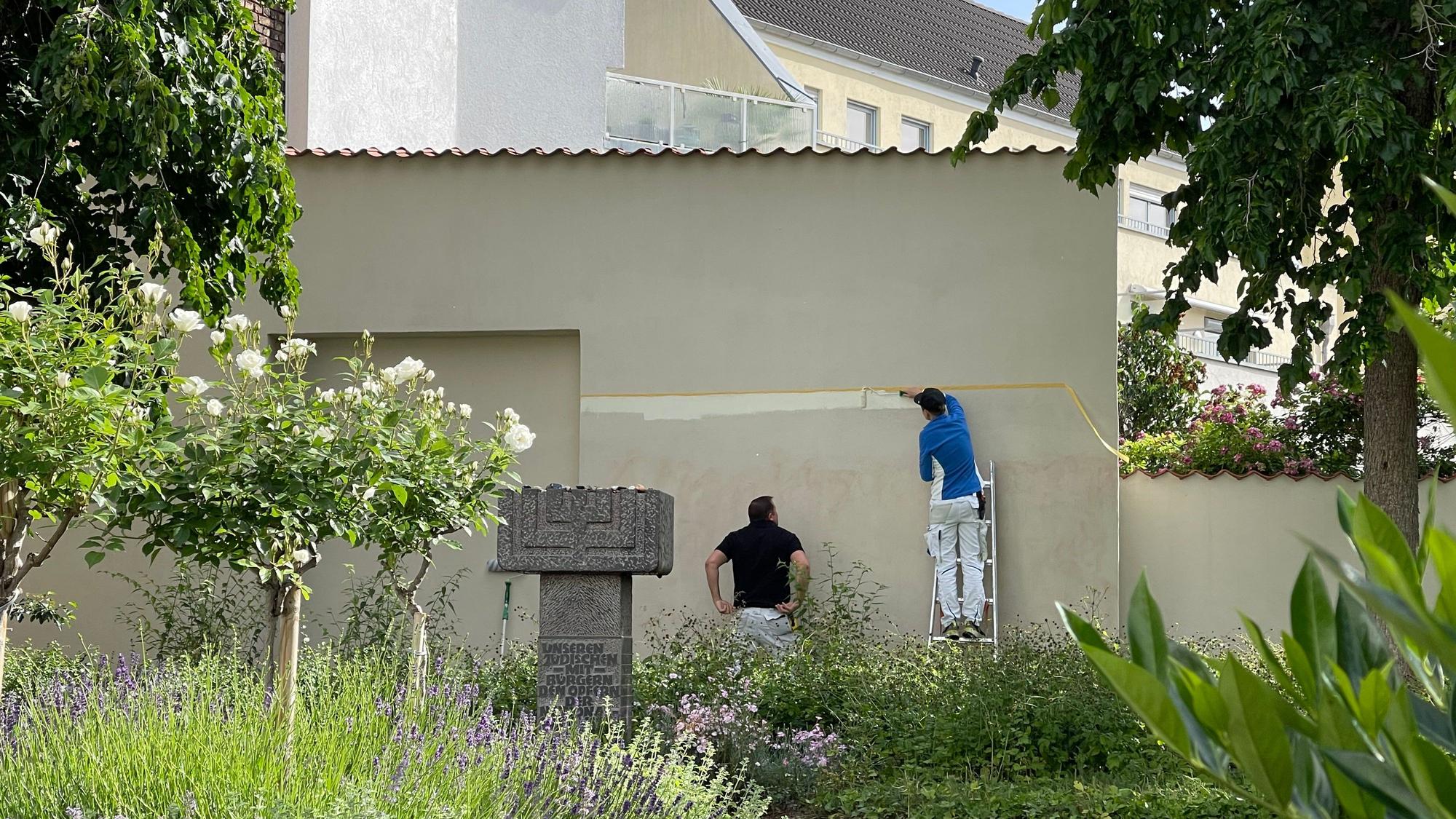 Ein Handwerker steht auf einer Leiter, seine Kollege sieht ihm bei der Arbeit zu.