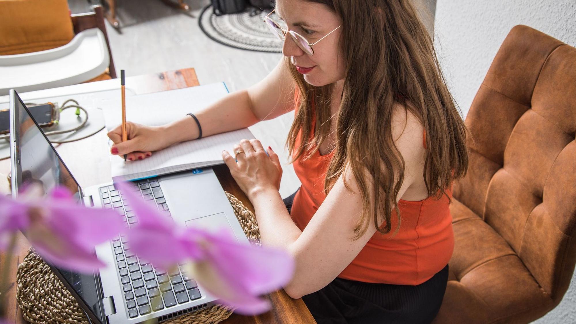 Eine Frau macht sich Notizen neben dem Laptop