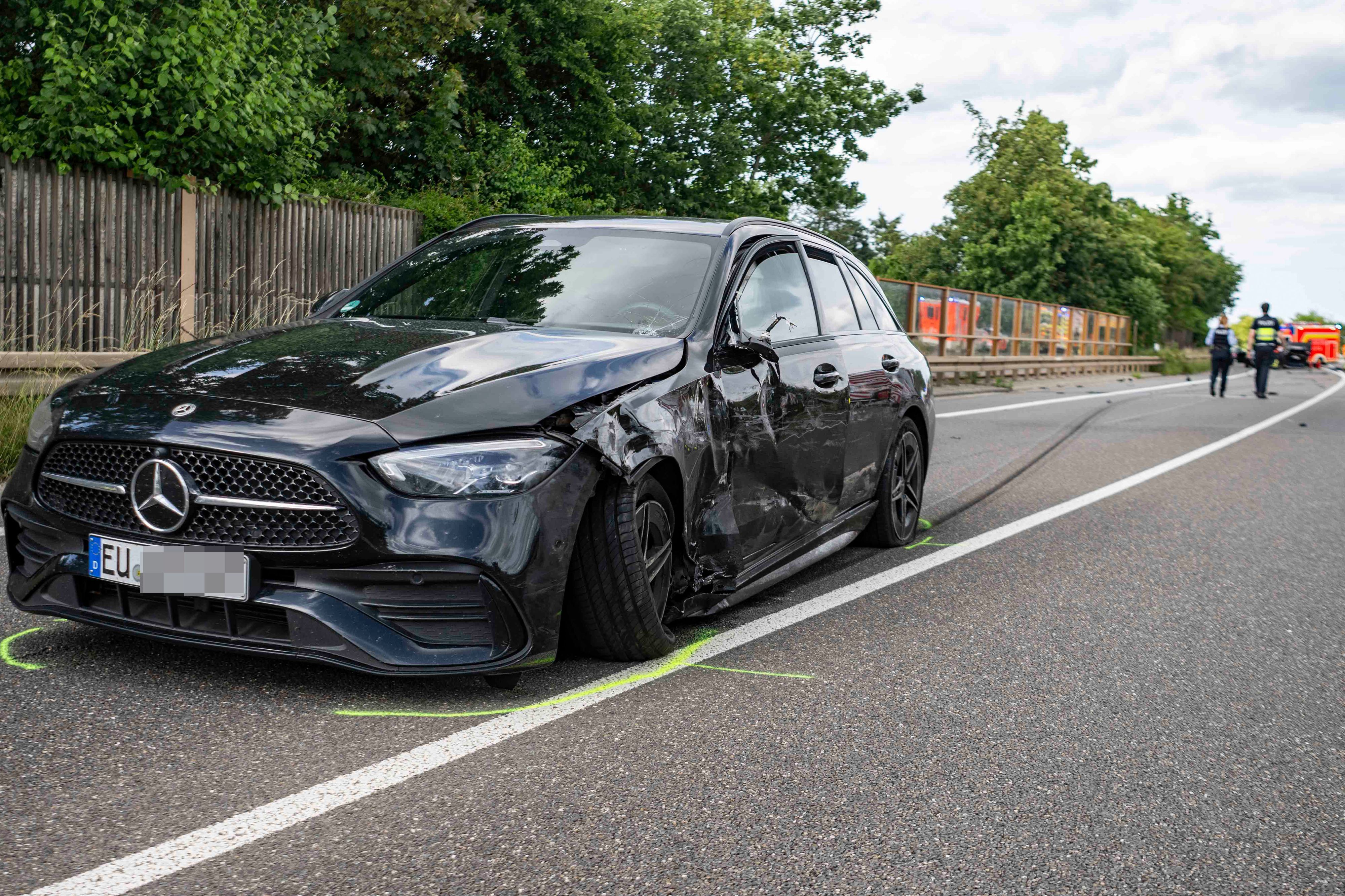 Das Bild zeigt einen schwarzen Mercedes, der im Bereich der Fahrerseite beschädigt ist.