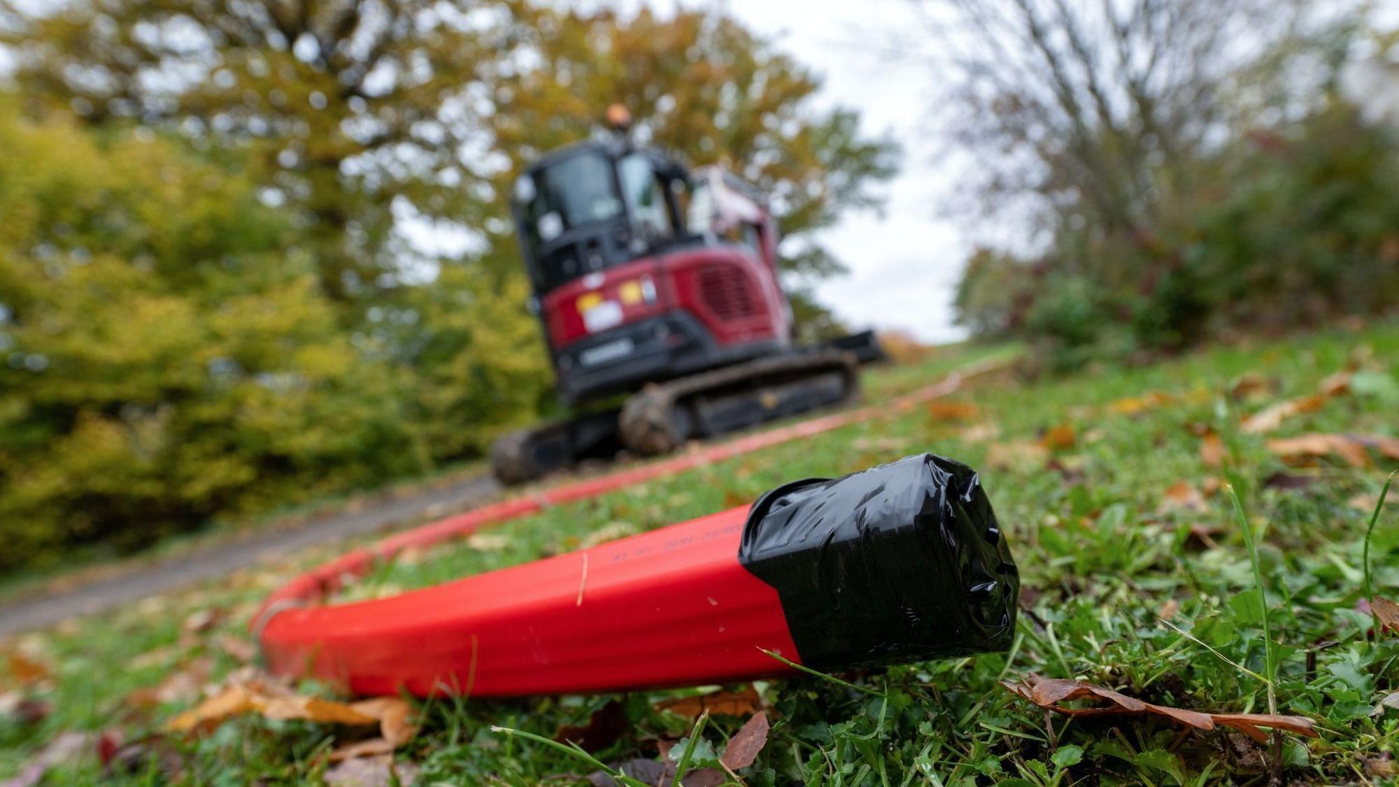 Ein Schutzrohr für Glasfaserkabel liegt vor einem Bagger