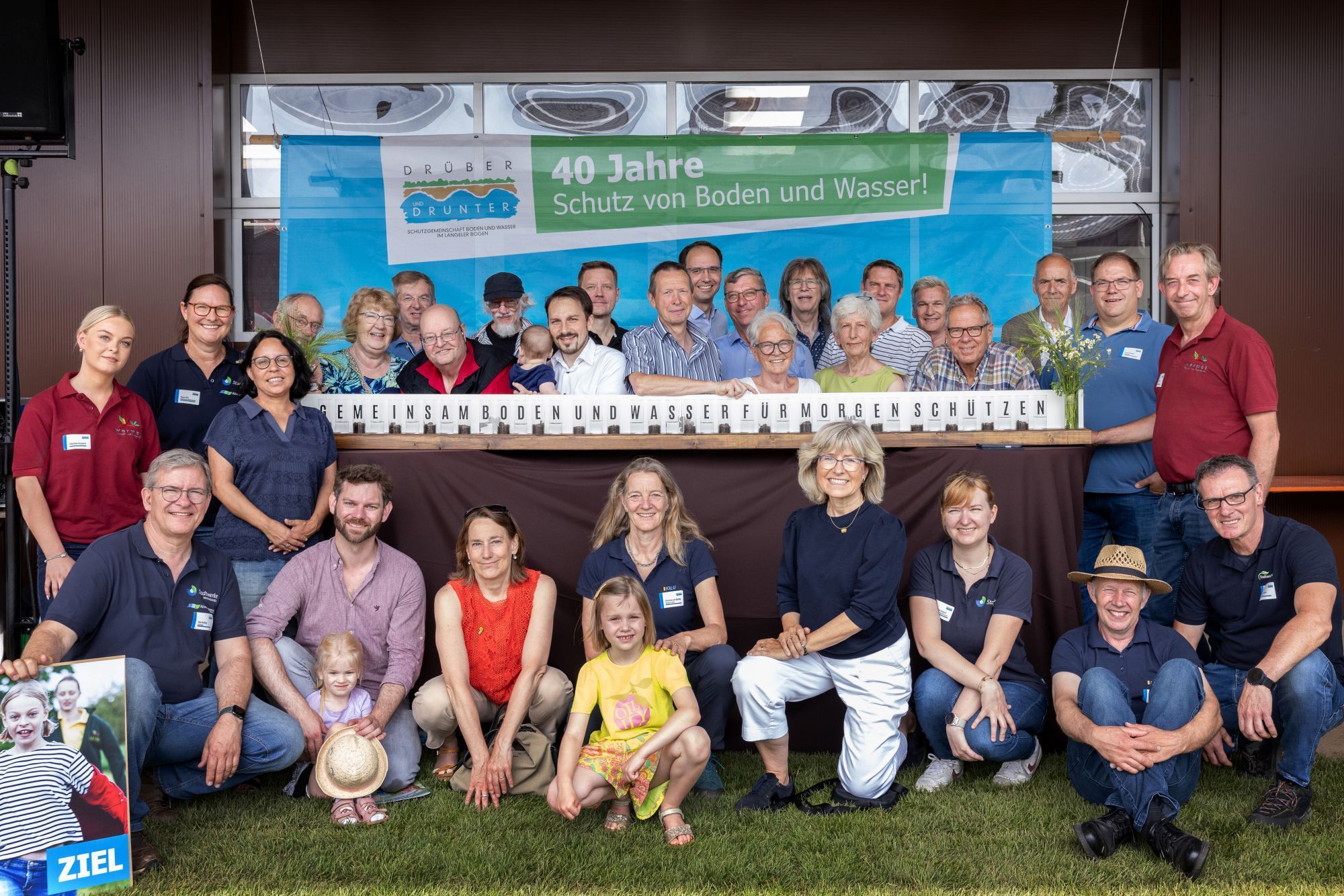 Viel Menschen stehen um einen Stand herum, auf dem der Slogan steht: Gemeinsam Boden und Wasser für morgen schützen.