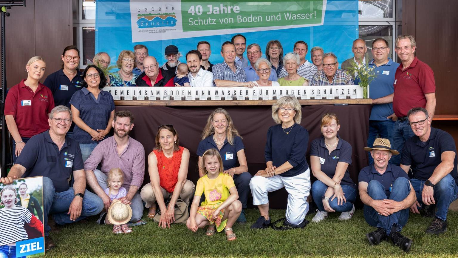 Viel Menschen stehen um einen Stand herum, auf dem der Slogan steht: Gemeinsam Boden und Wasser für morgen schützen.