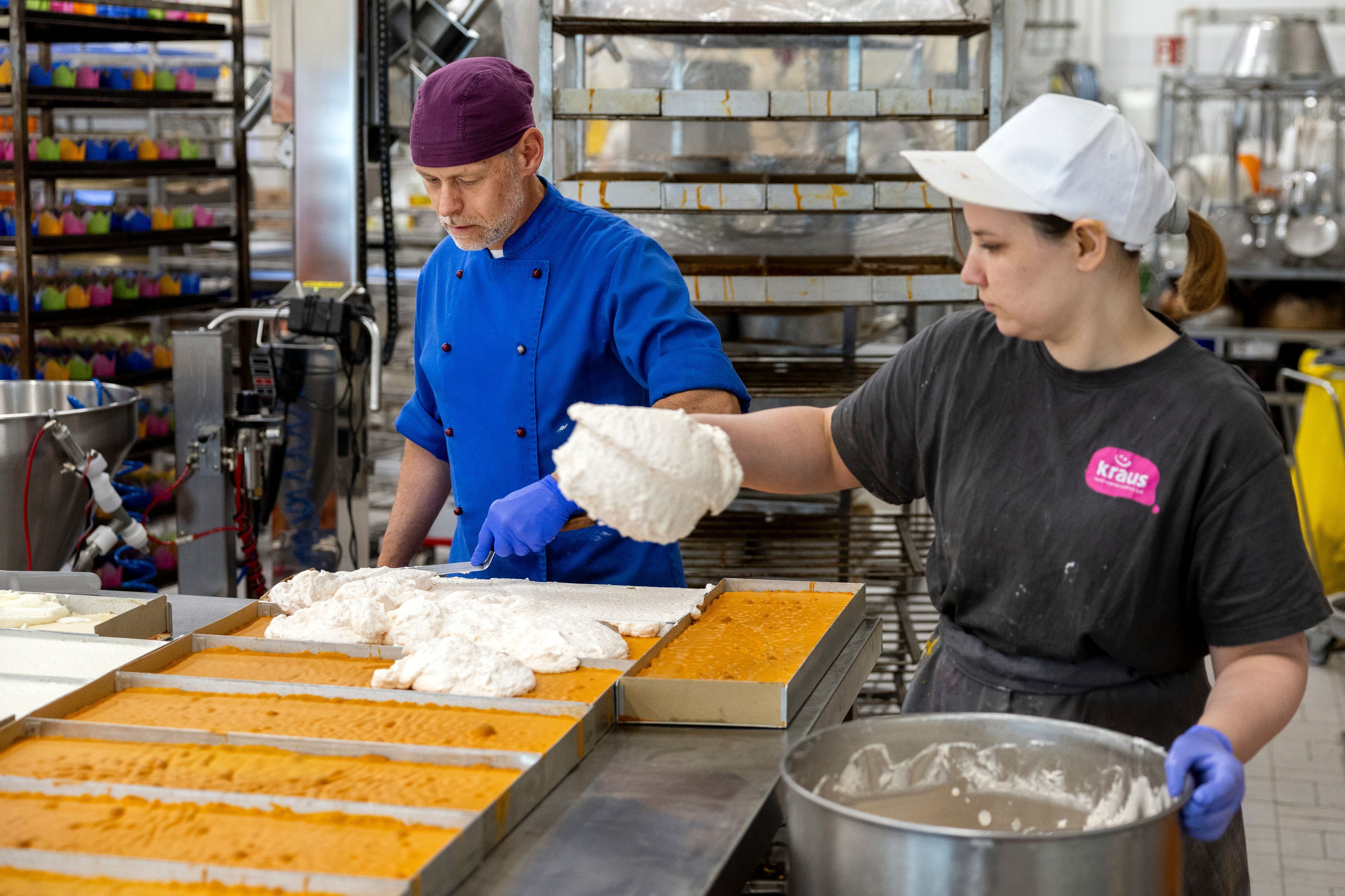 Zwei Mitarbeitende belegen Kuchenböden in eckigen Formen mit einer Sahnemasse.