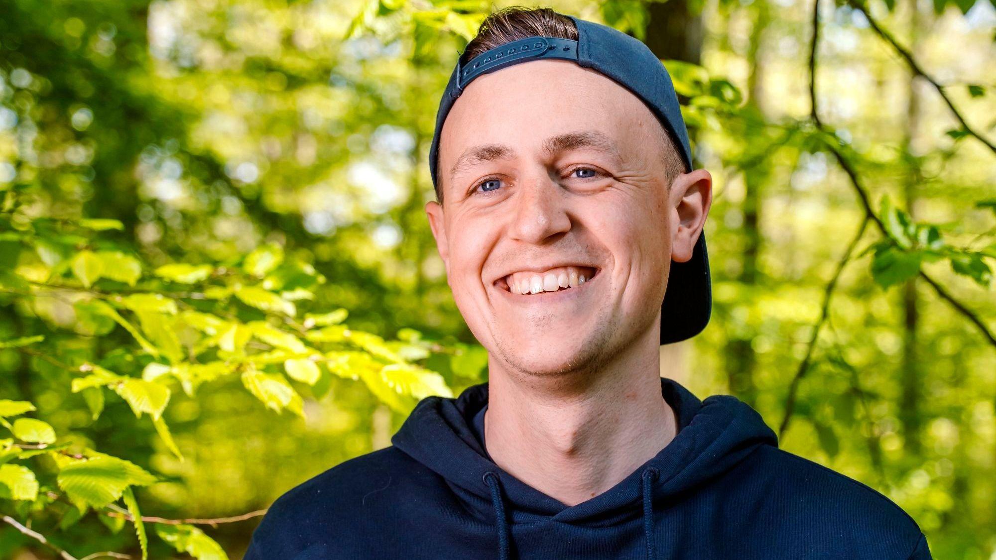Tobias Wohlleben steht im Wald, er trägt eine Kappe verkehrt herum.