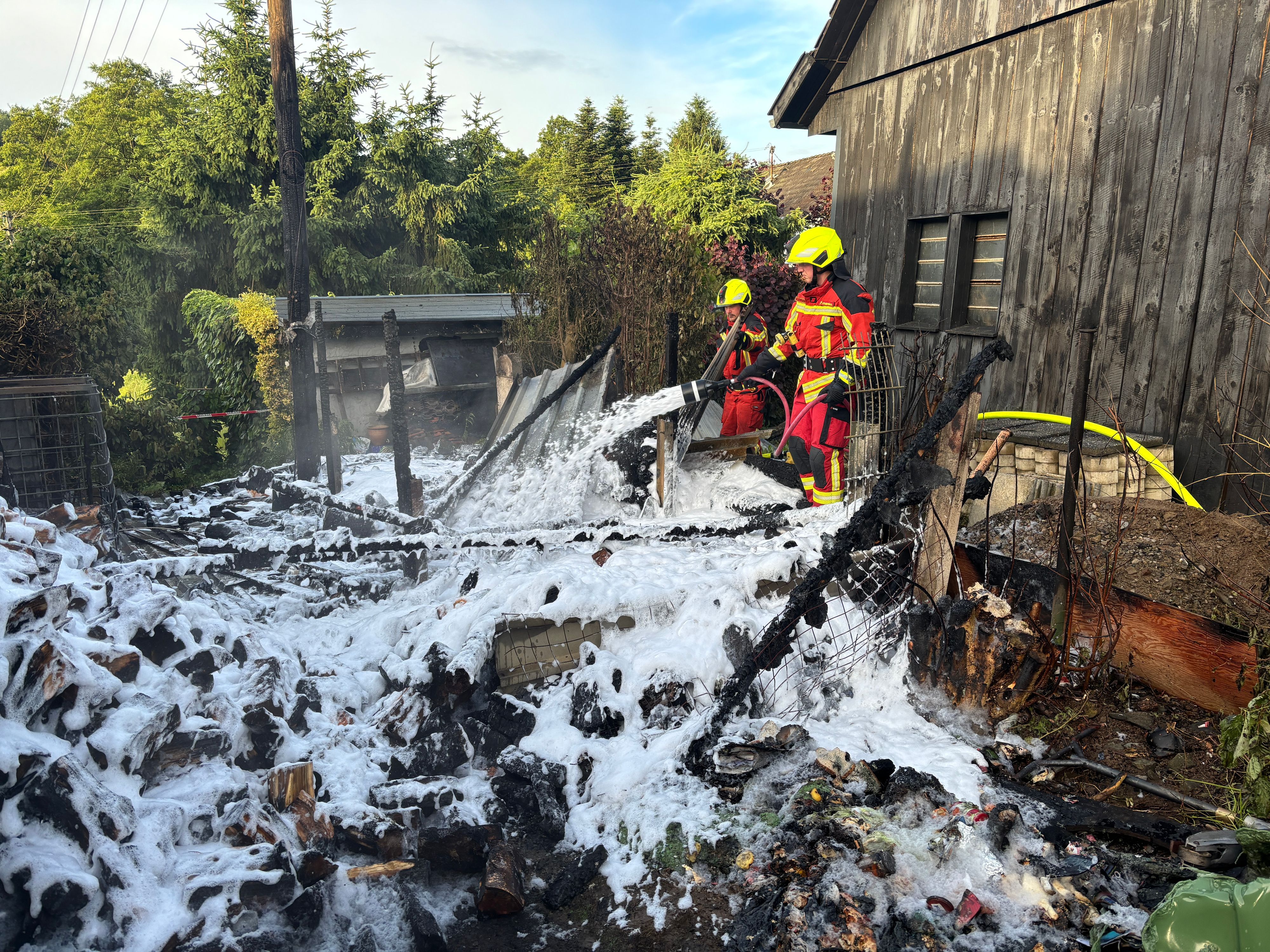 Das Foto zeigt die Reste eines abgebrannten Schuppens und zwei Feuerwehrleute