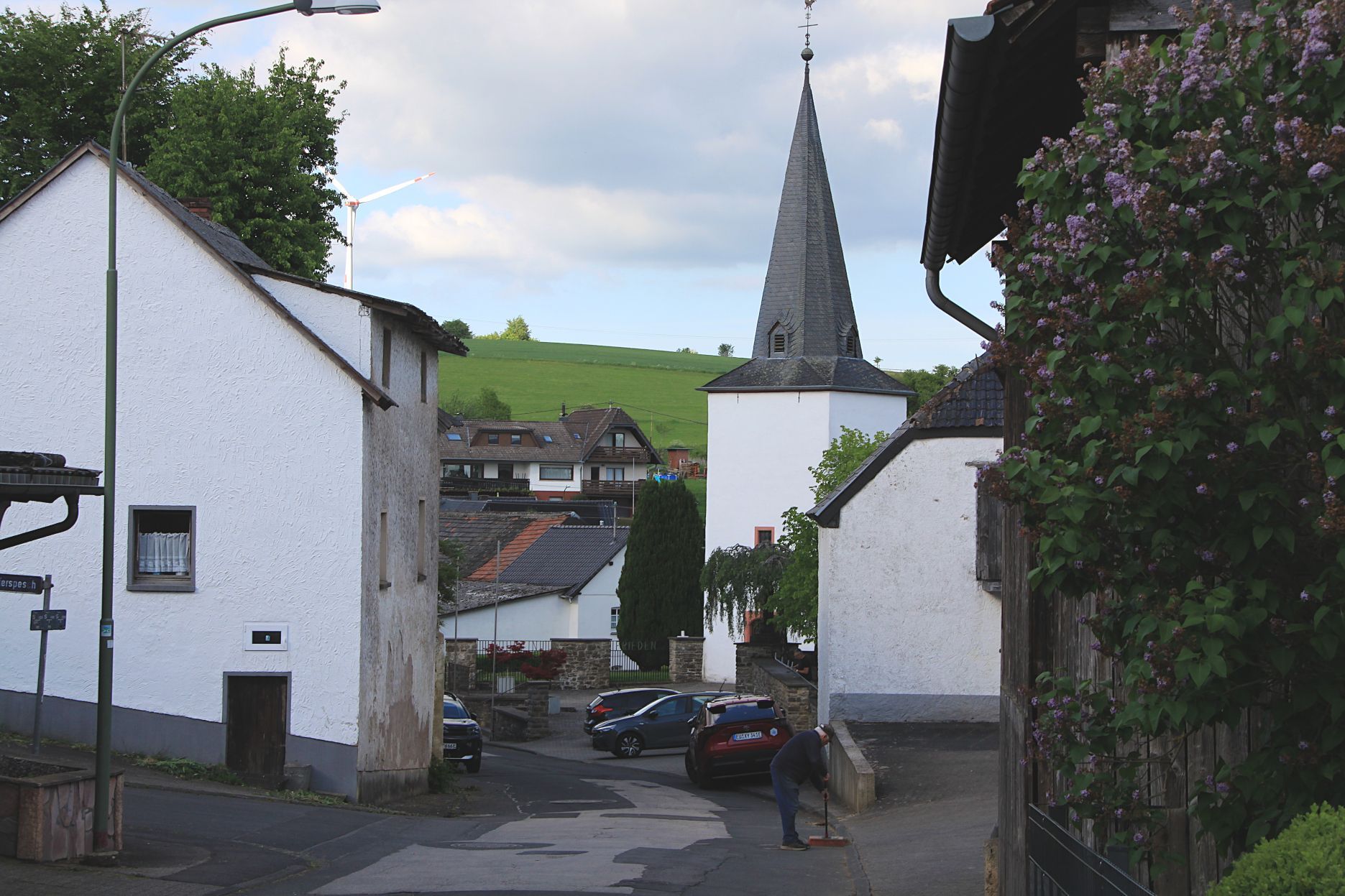 Das Foto zeigt die Kirche in Reetz, drumherum stehen Häuser, auf einem Hügel steht ein Windrad.