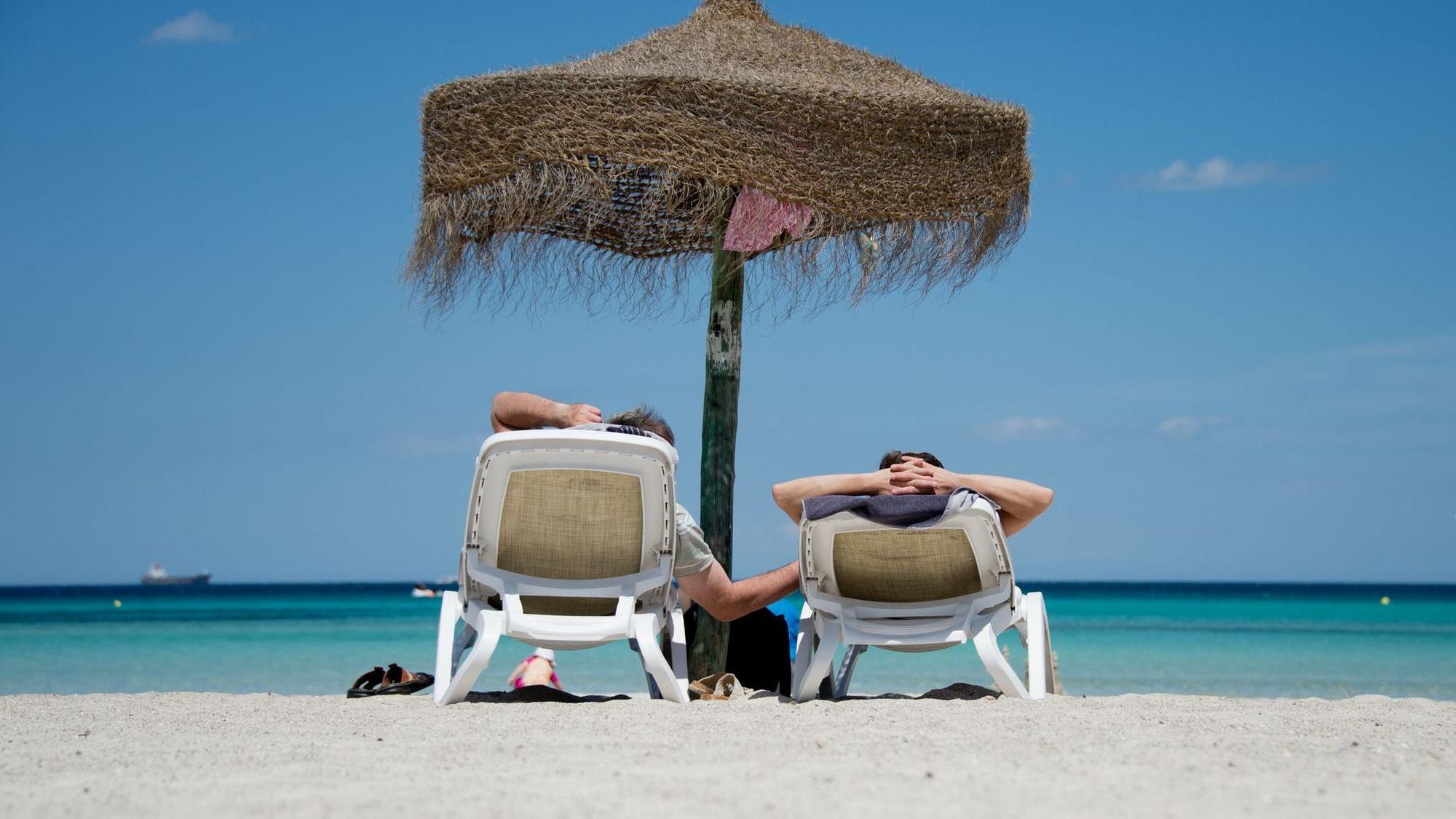 Touristen liegen am Strand unter einem Sonnenschirm