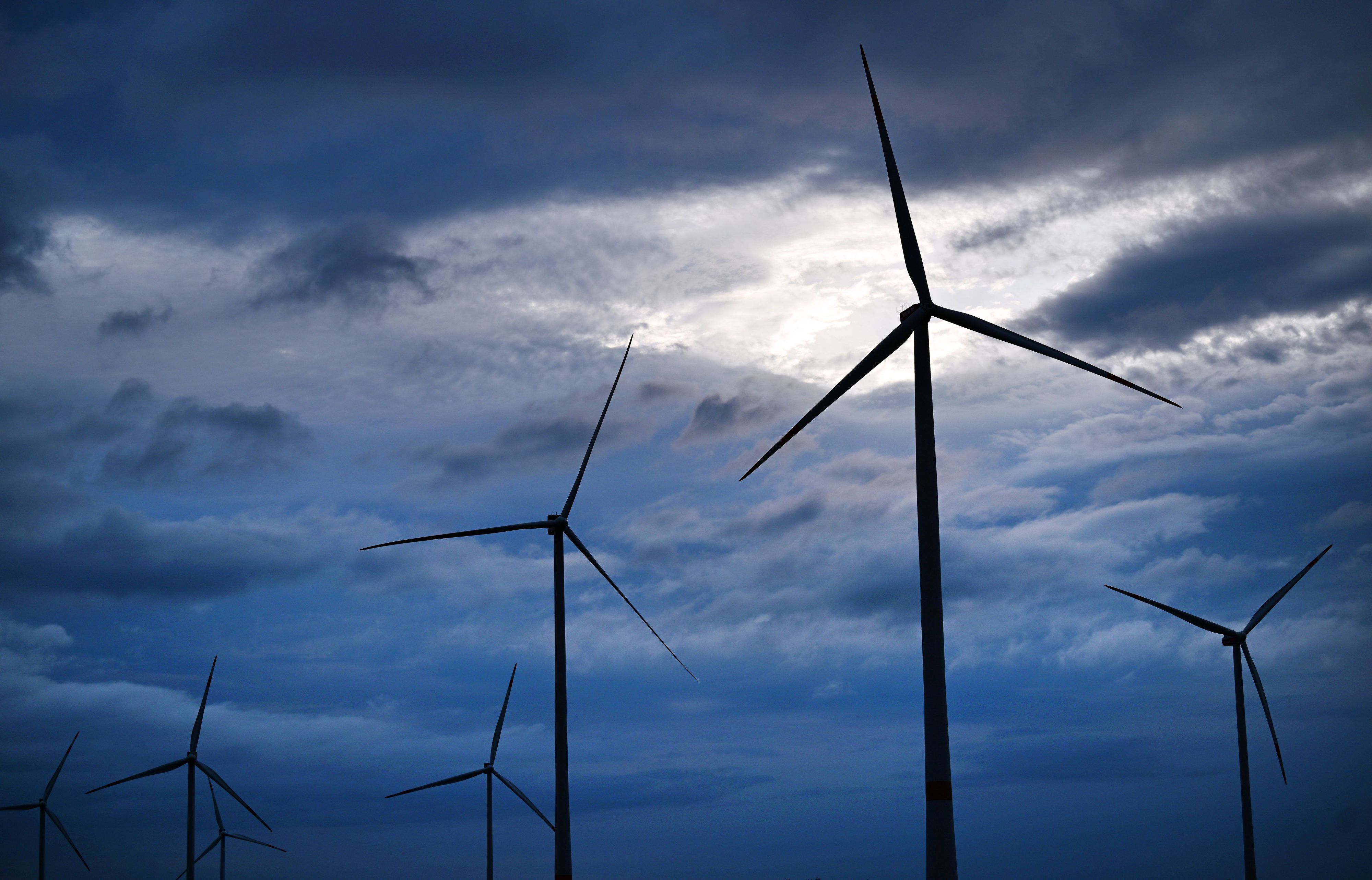 Über einem Windpark bei Gotha scheint Sonnenlicht zwischen dunklen Regenwolken hindurch.