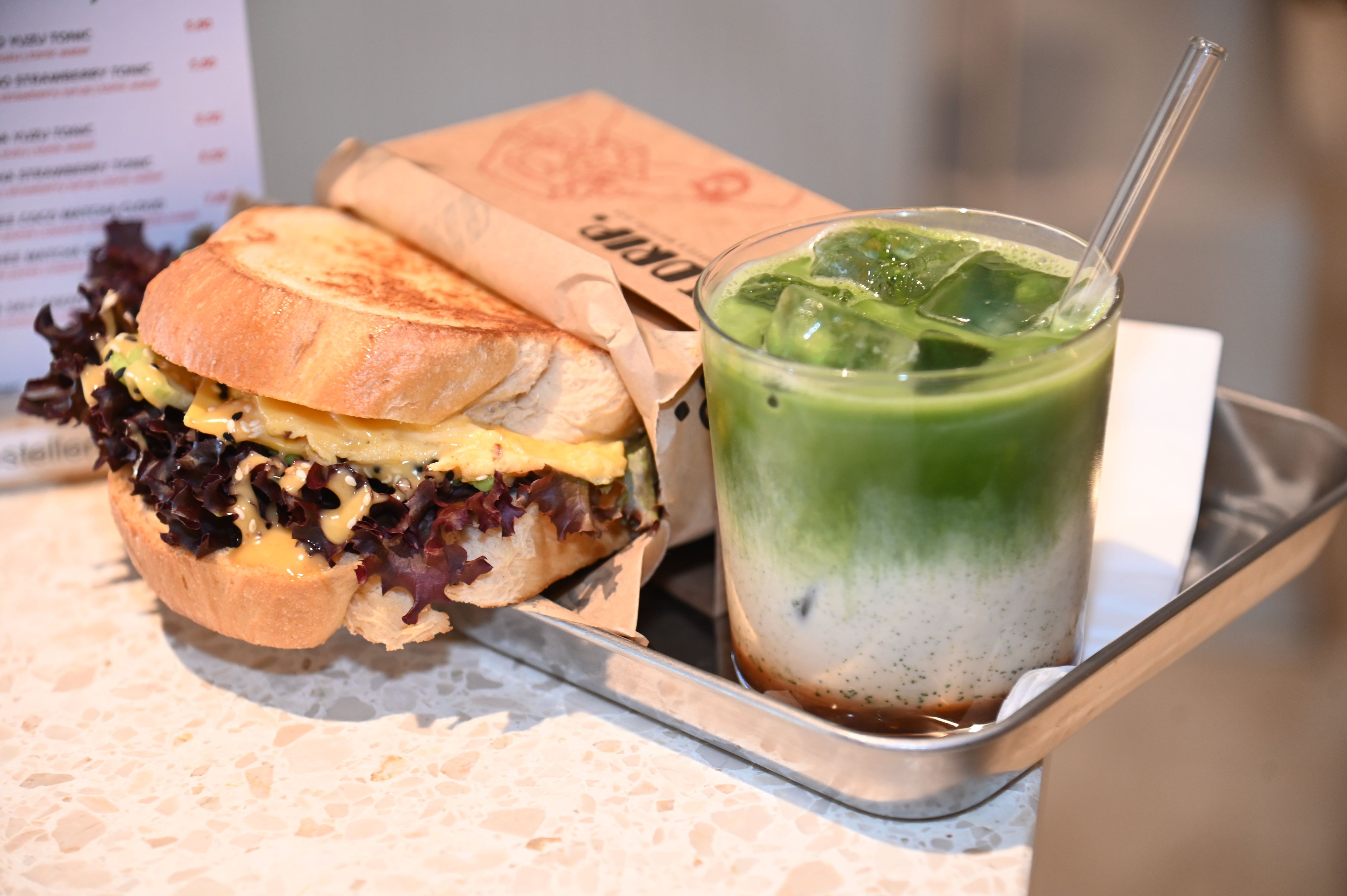 Ein Sandwich und ein Iced-Matcha-Latte, serviert auf einem silbernen, eckigen Tablett
