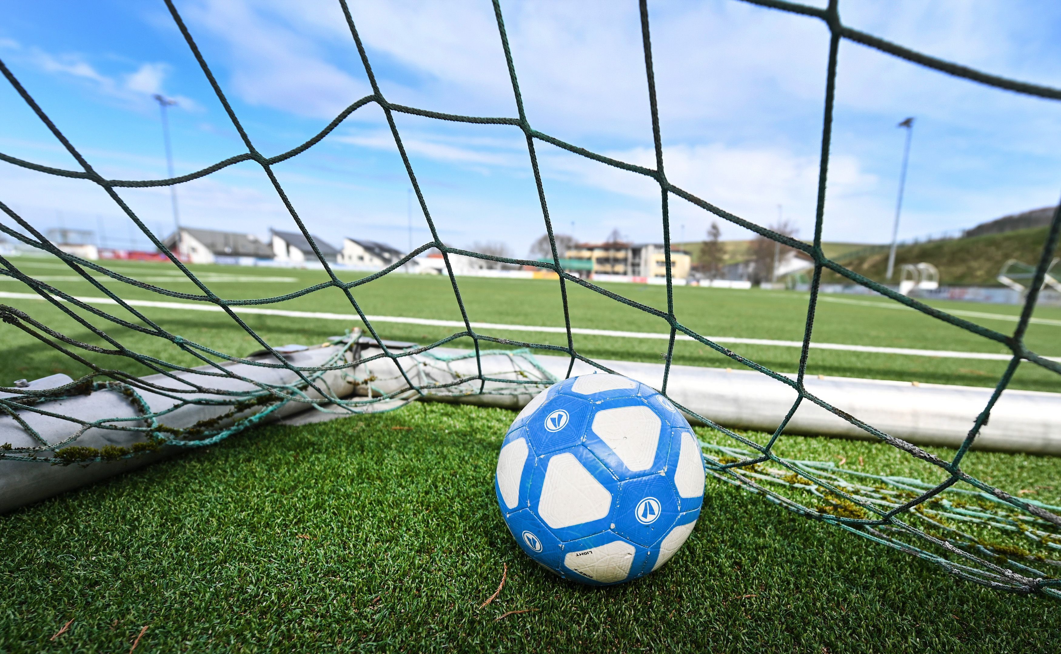Ein Fußball liegt in einem Tor, das auf einem leeren Fußballplatz steht.