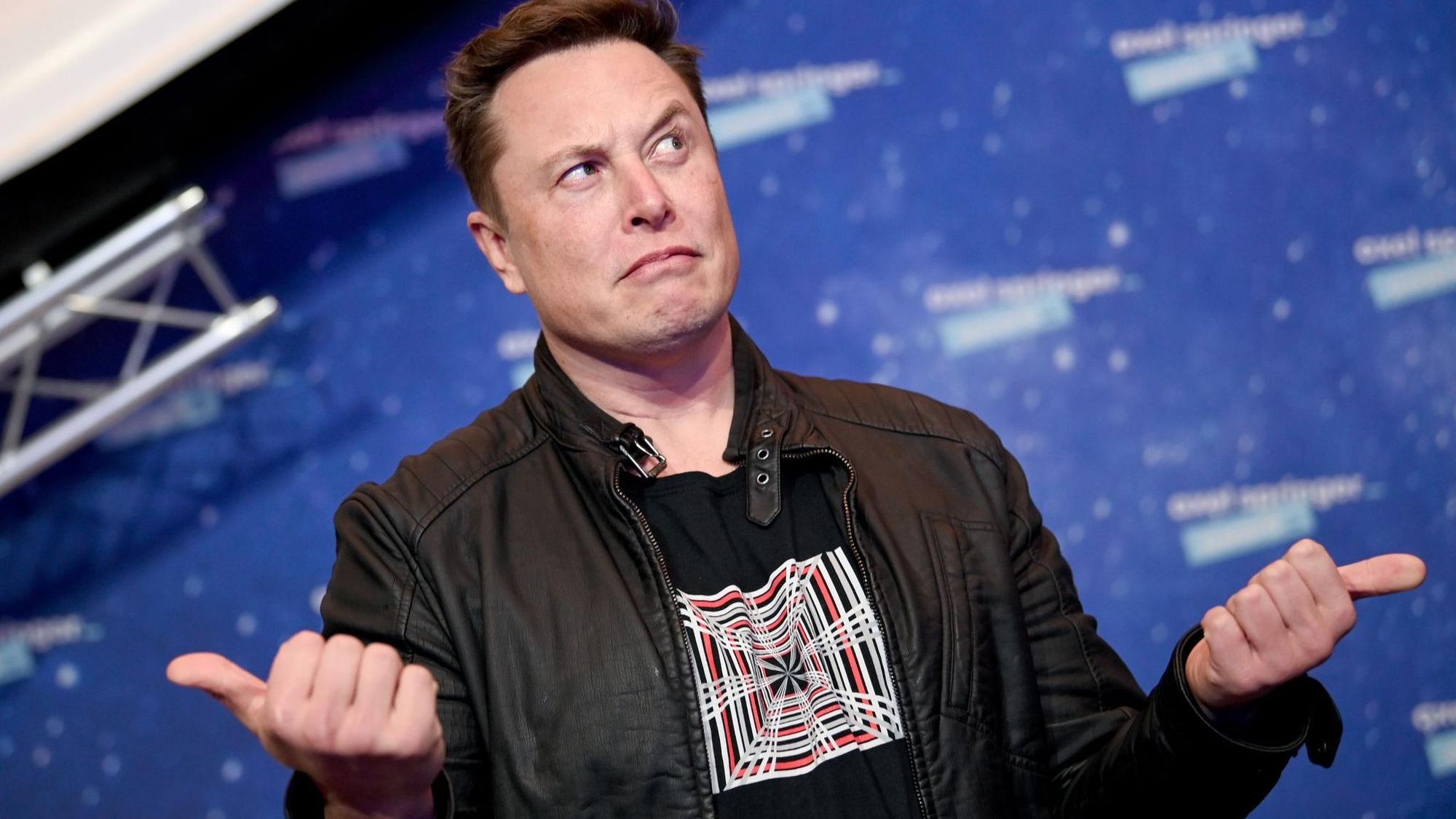 Elon Musk, Chef von SpaceX, guckt fragend vor einer Fotowand