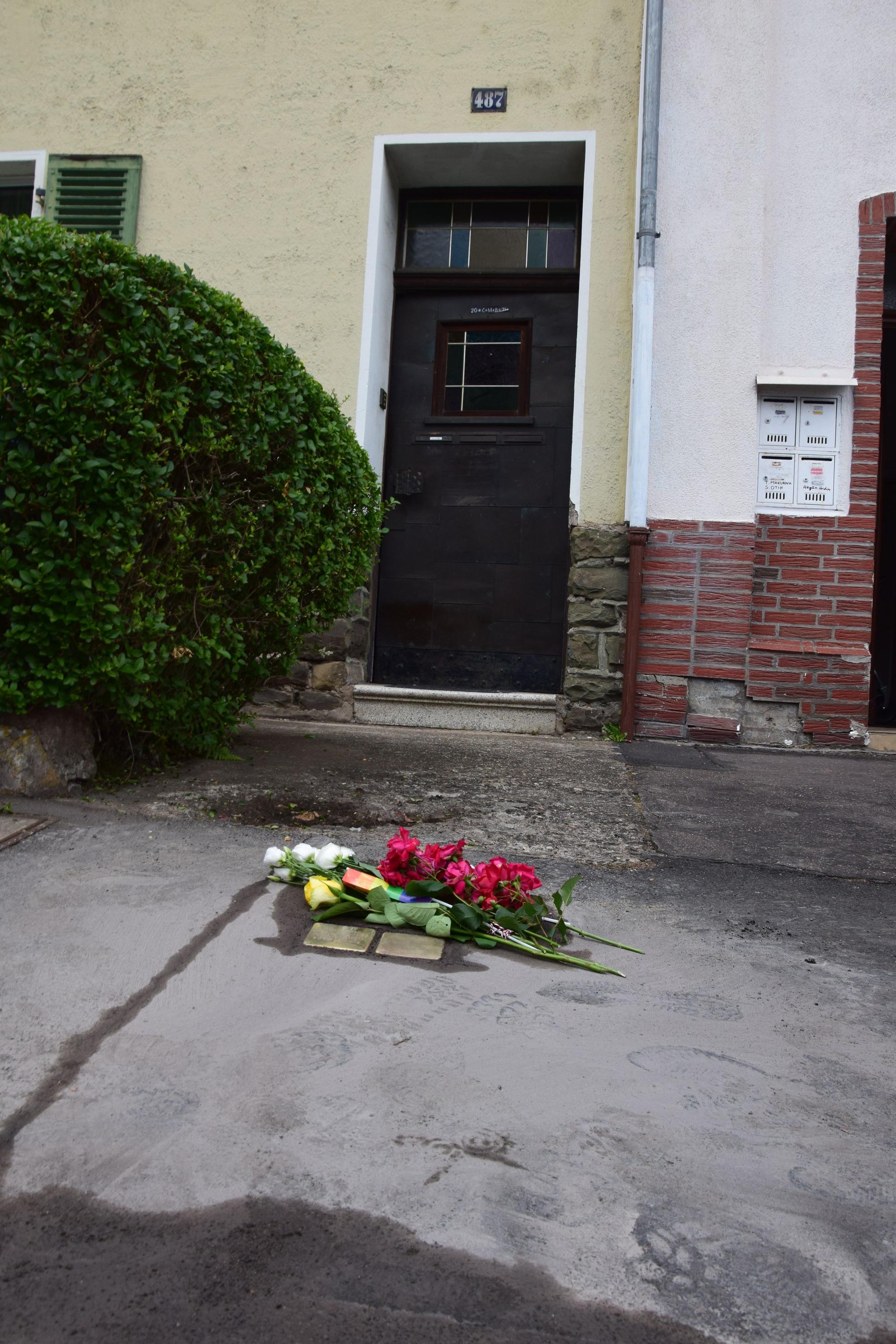 Vor einem Reihenhaus sind frisch verlegte Stolpersteine zu sehen. Darauf liegen Rosen und Regenbogenfähnchen.