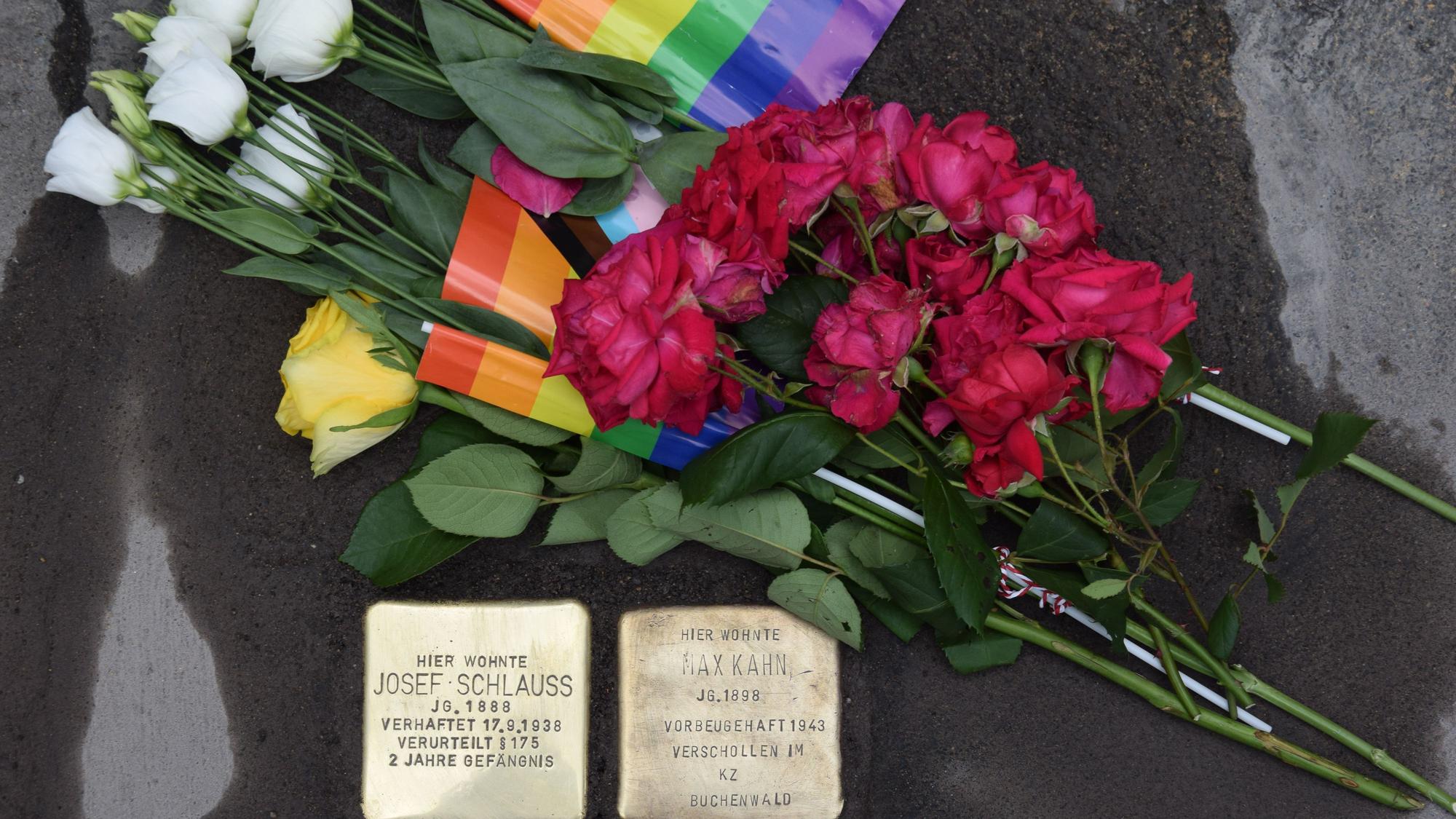 Auf zwei neu verlegten Stolpersteinen liegen Rosen und Regenbogen-Fähnchen.