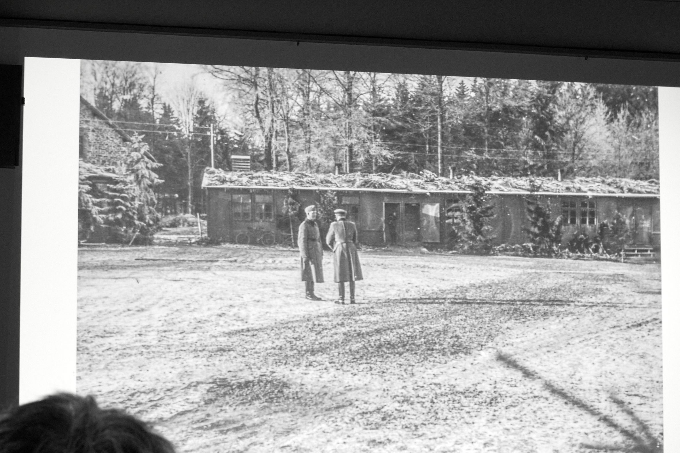 Ein hostorisches Foto zeigt zwei Männer in Uniformmantel vor einer Baracke des Kriegsgefangenenlagers in Hellenthal-Hollerath.