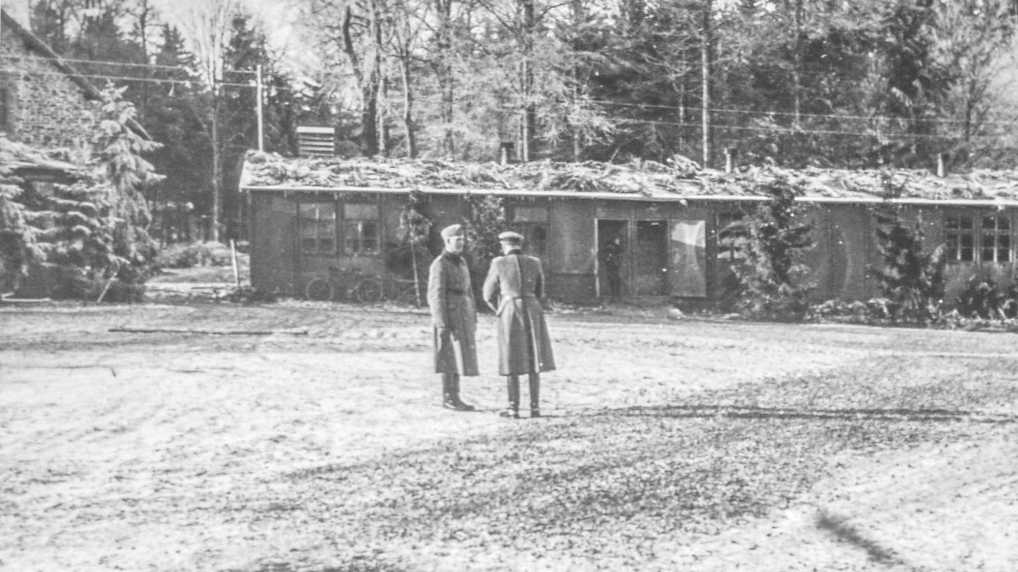 Ein hostorisches Foto zeigt zwei Männer in Uniformmantel vor einer Baracke des Kriegsgefangenenlagers in Hellenthal-Hollerath.