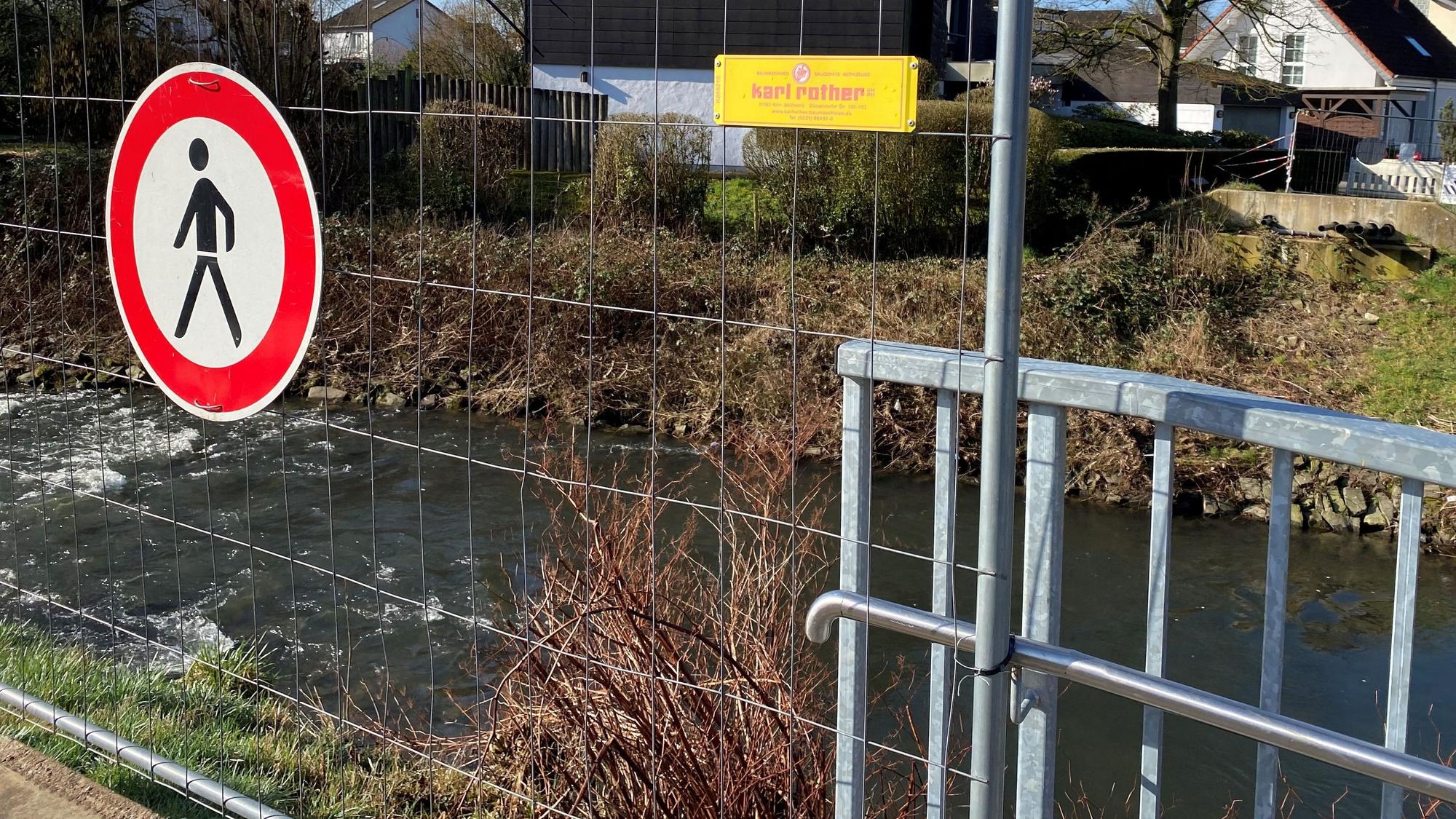 Eine Absperrung für Fußgänger, dahinter ein Fluss, am anderen Ufer kann man Betonreste sehen von der abgerissenen Mauer