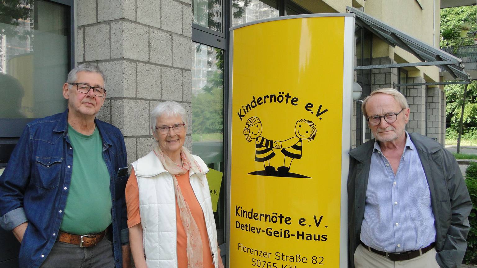 Zwei Männer und eine Frau stehen links und rechts von einer gelben Säule, auf der Kindernöte e.V., steht.
