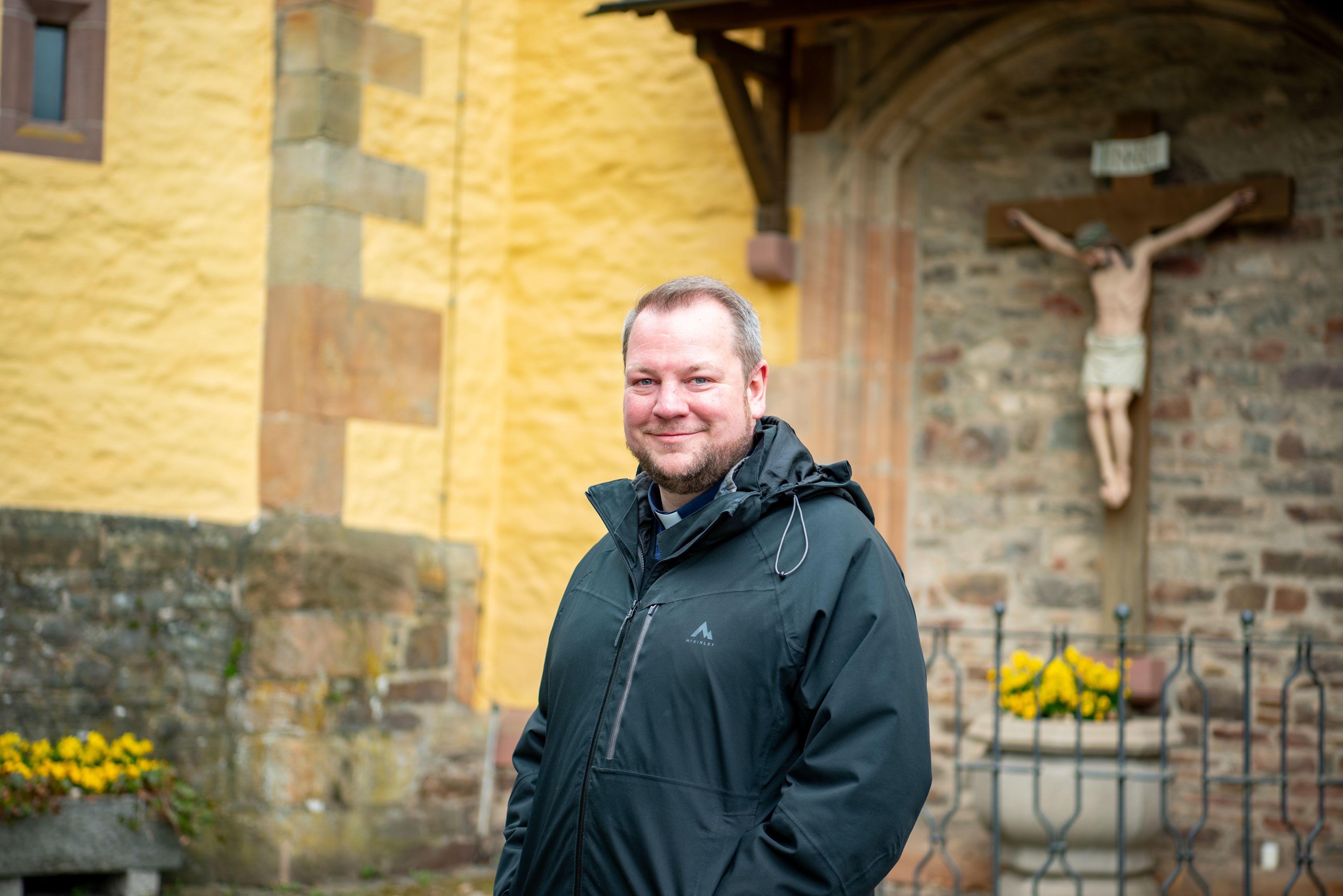 Pfarrer Thomas Schlütter steht in schwarzer Regenjacke vor der Schlosskirche in Schleiden.