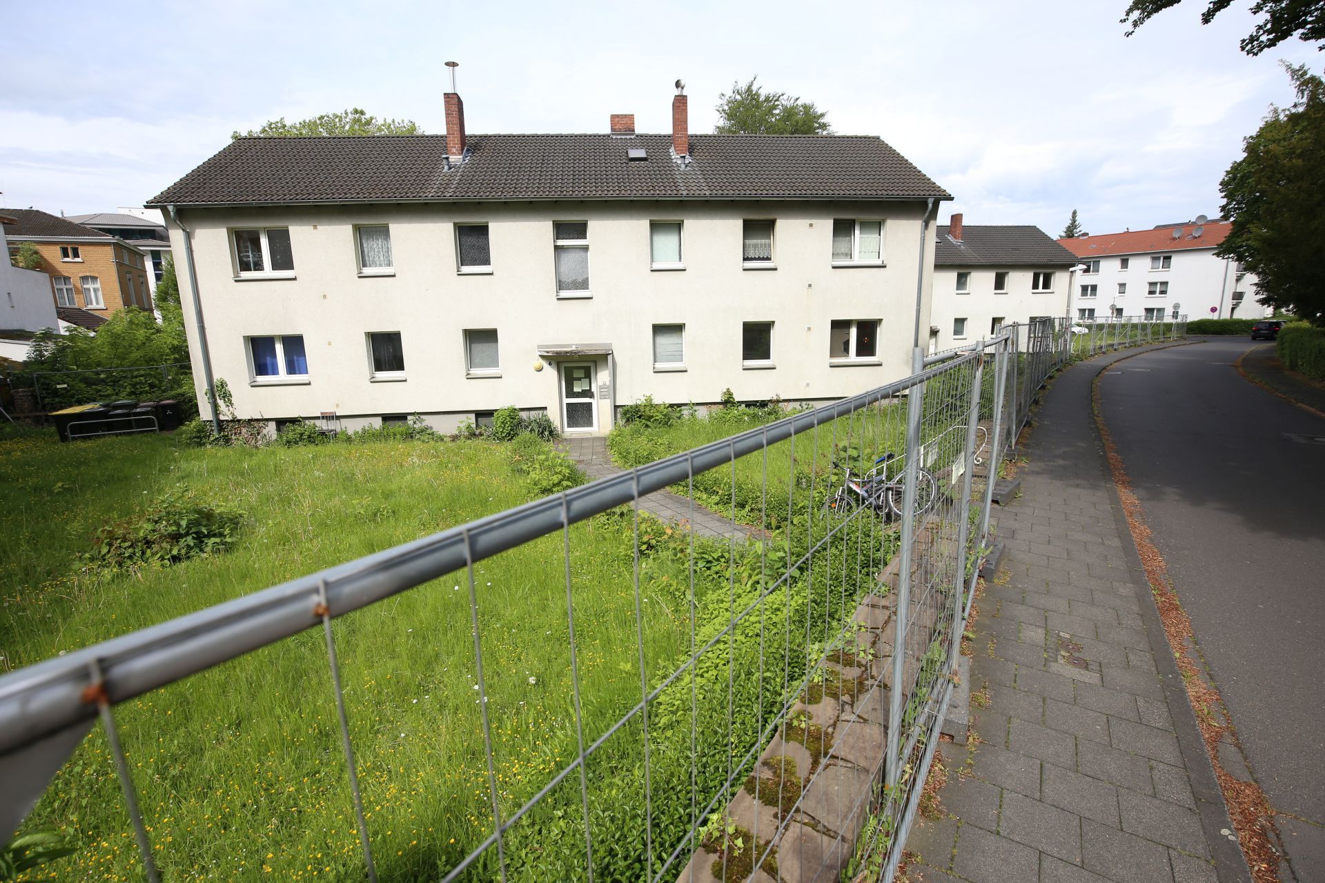 Ein zweistöckiges Mehrfamilienhaus, davor ein Wiese und ein Bauzaun.