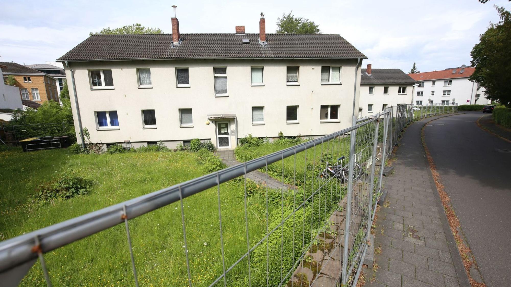 Ein zweistöckiges Mehrfamilienhaus, davor ein Wiese und ein Bauzaun.