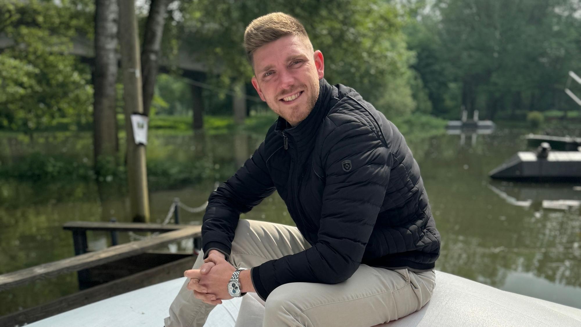 Felix Heyne sitzt auf einem Steg an der Sieg und lächelt in die Kamera.