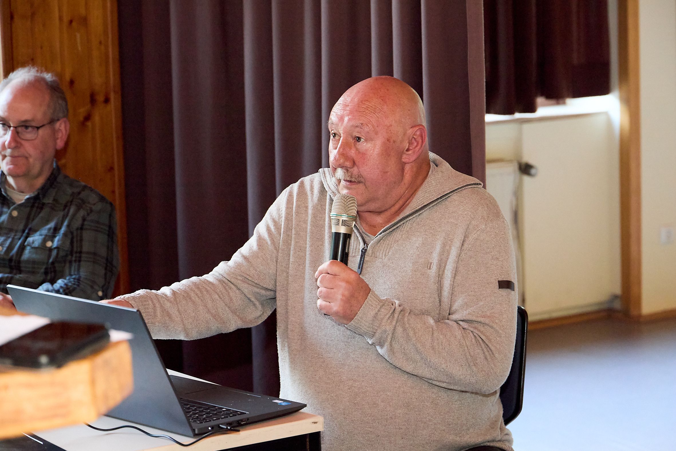 Journalist F.A. Heinen sitzt in einem hellen Pullover vor einem Laptop und spricht in ein Mikrofon.