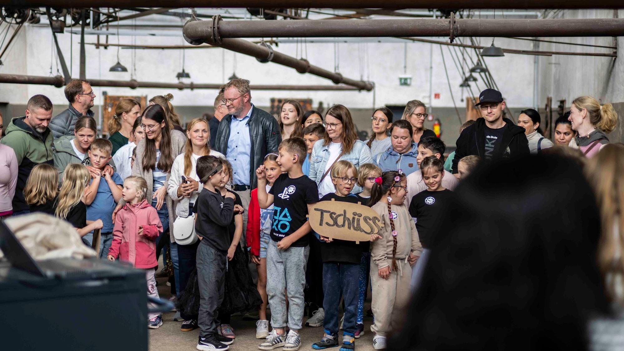 Eine Gruppe Kinder steht zusammen. Ein Kind hält ein Pappschild in der Hand, auf dem steht: „Tschüss“.