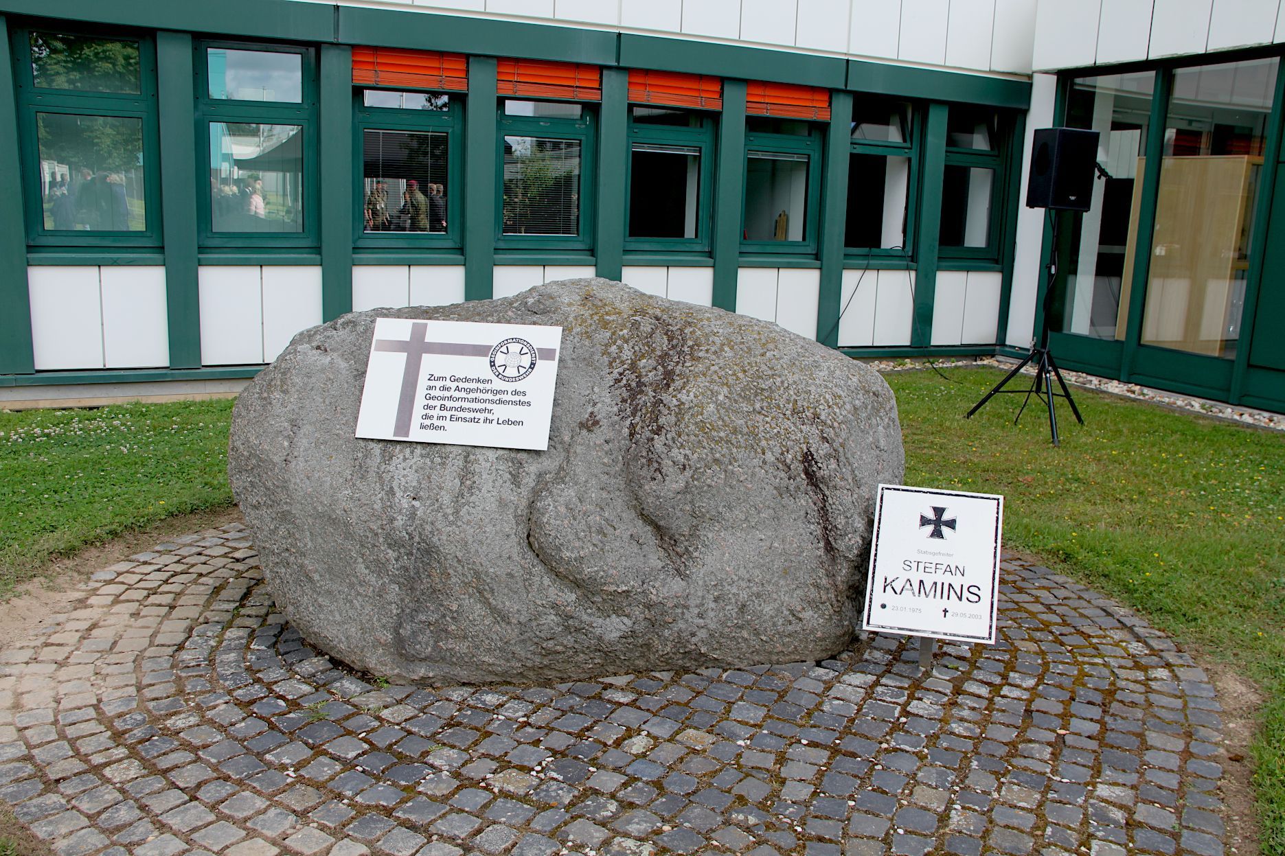 In einem Innhof steht ein Stein, an dem zwei Gedenktafeln angebracht sind.