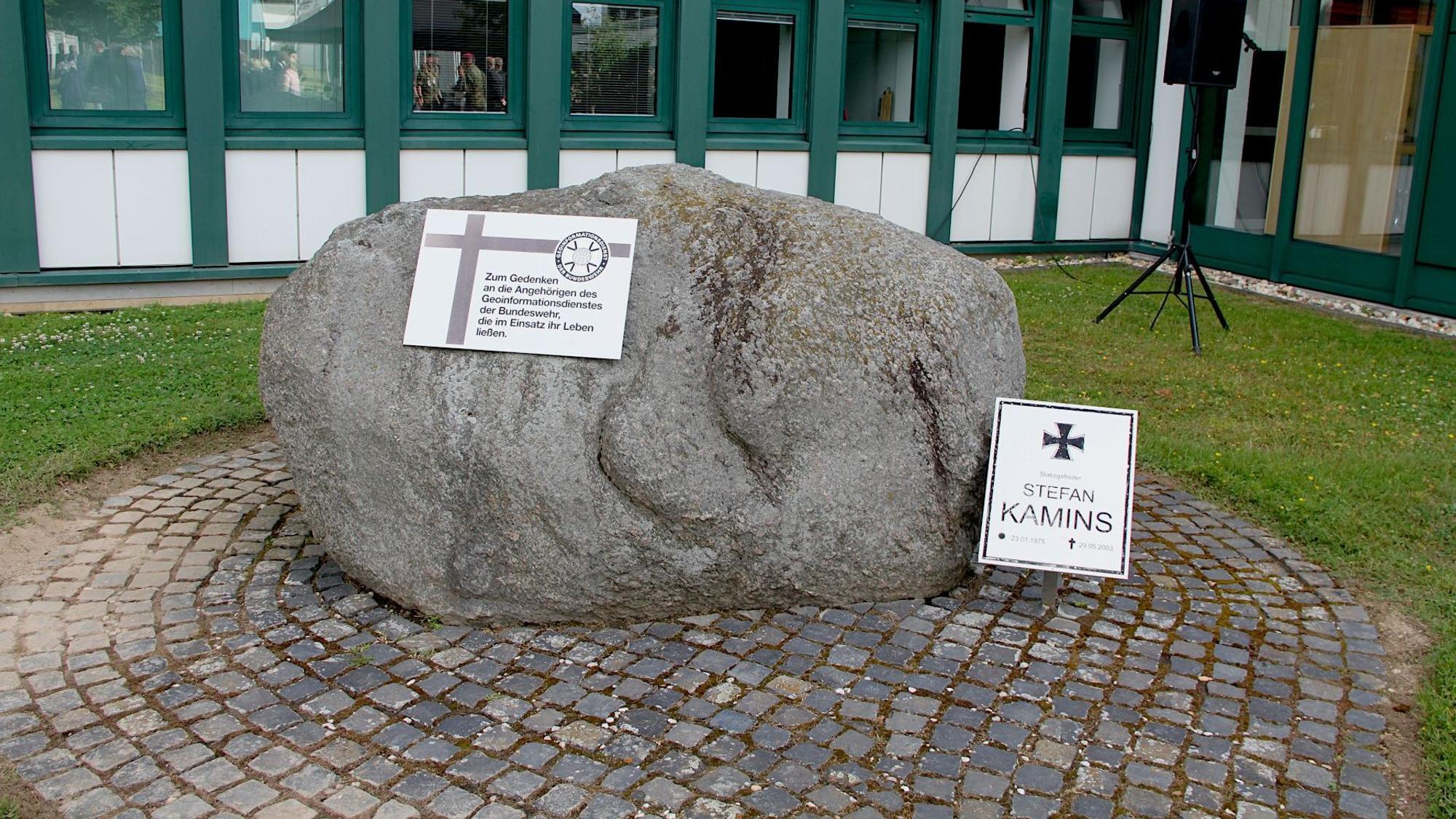 In einem Innhof steht ein Stein, an dem zwei Gedenktafeln angebracht sind.