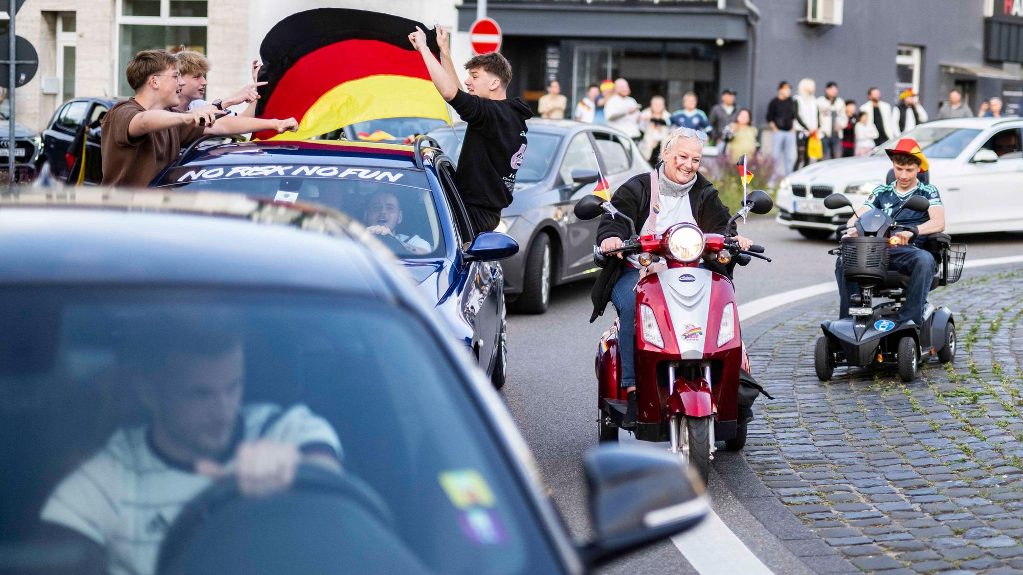 Eine Frau und ein junger Mann fahren mit Elektromobilen am Autokorso vorbei.
