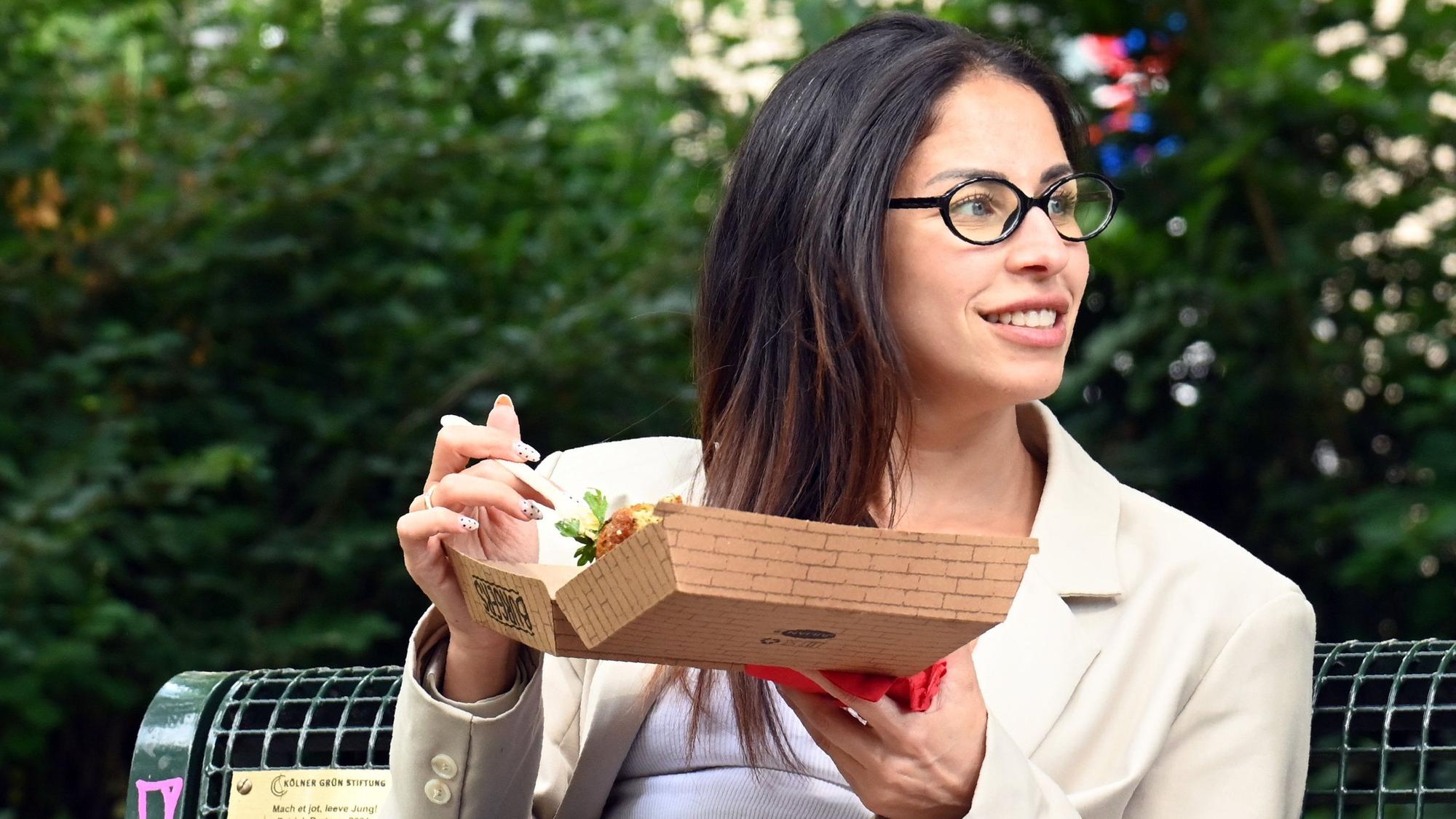 Eine junge Frau sitzt auf einer Bank mit einer Box in der Hand.