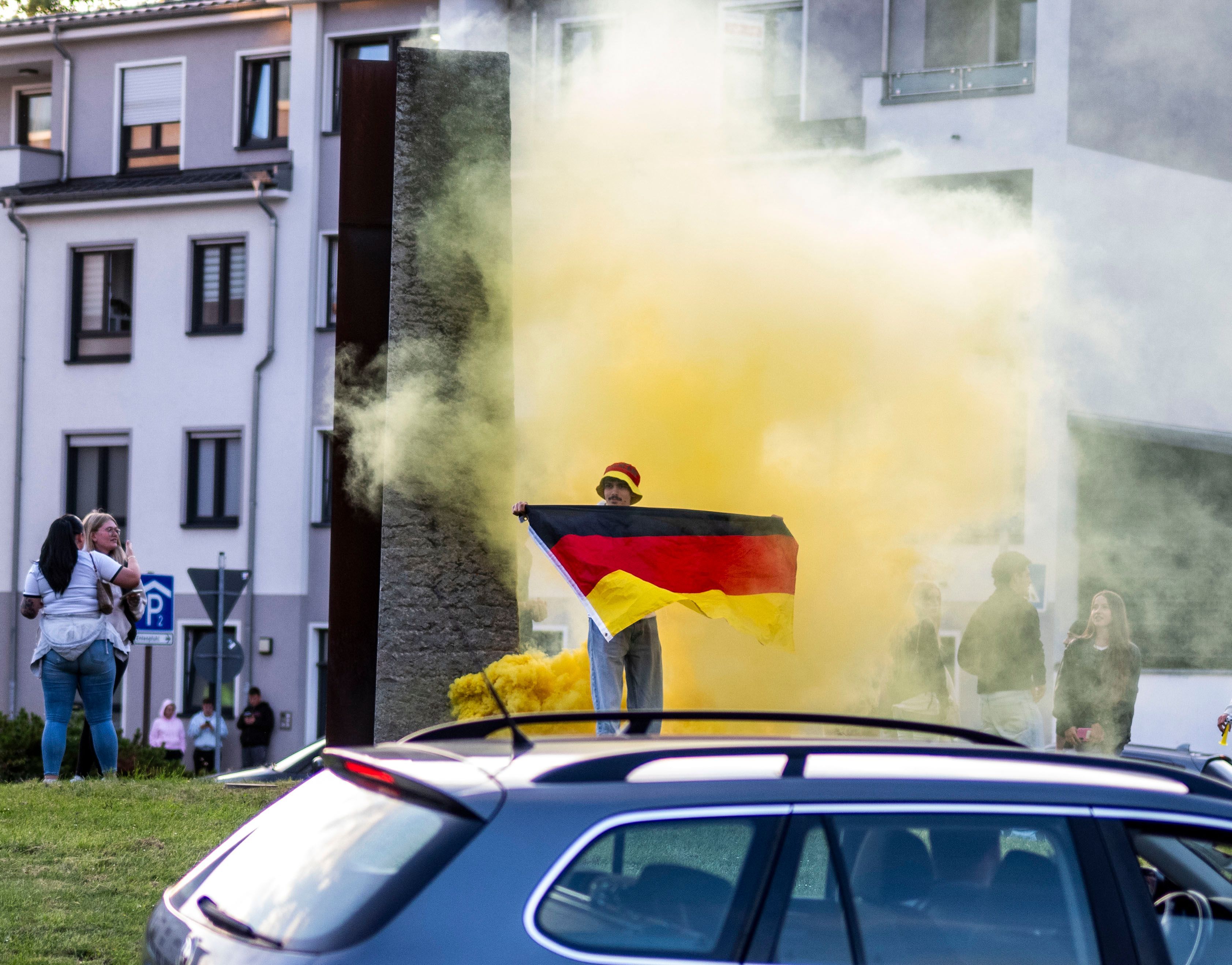 Ein Mann hält eine Deutschland-Fahne vor die Brust, im Hintergrund ist gelber Rauch zu erkennen.