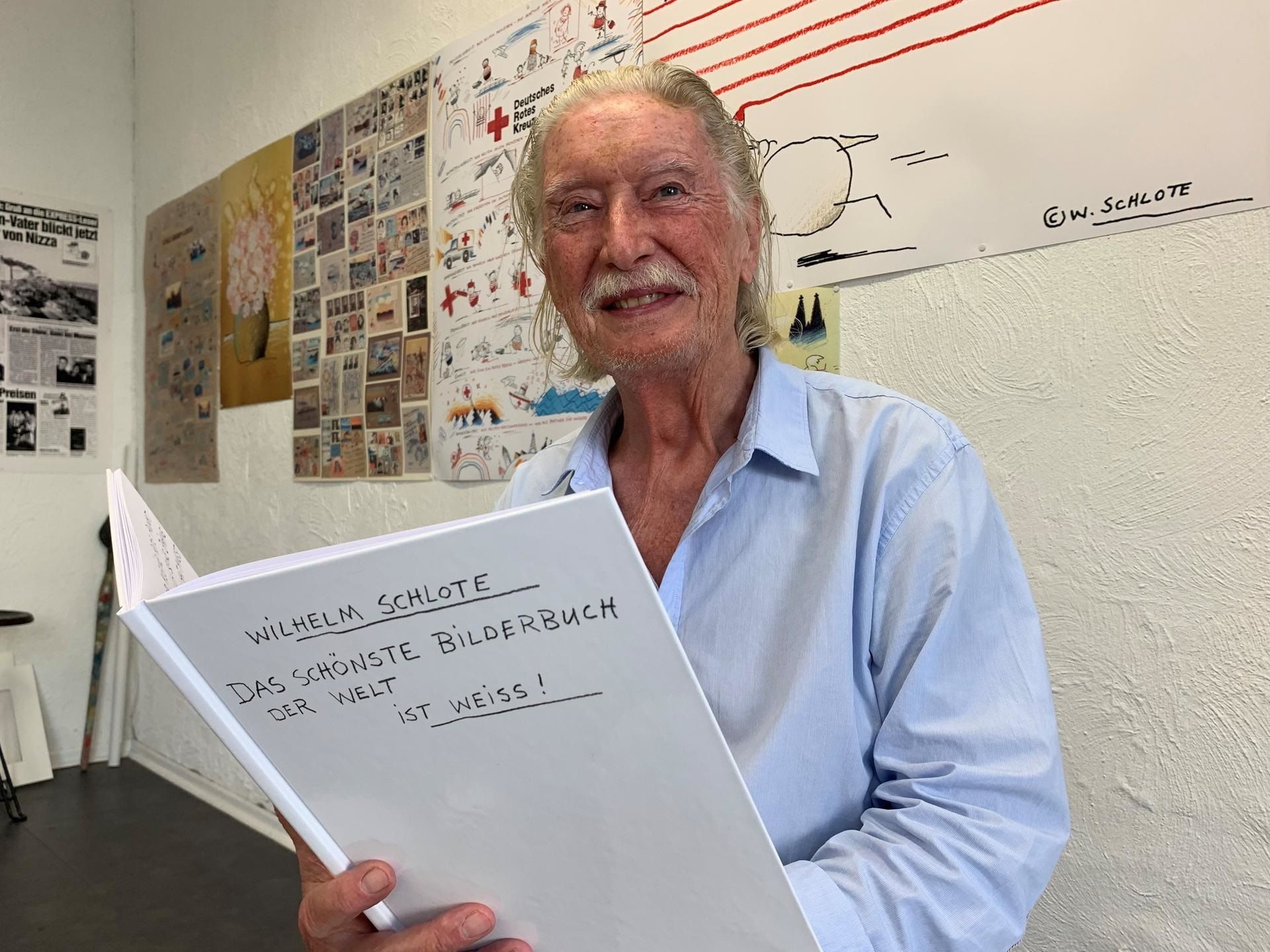 Ein alter Mann mit weißem Haar und Schurrbart hält ein weißes Buch.