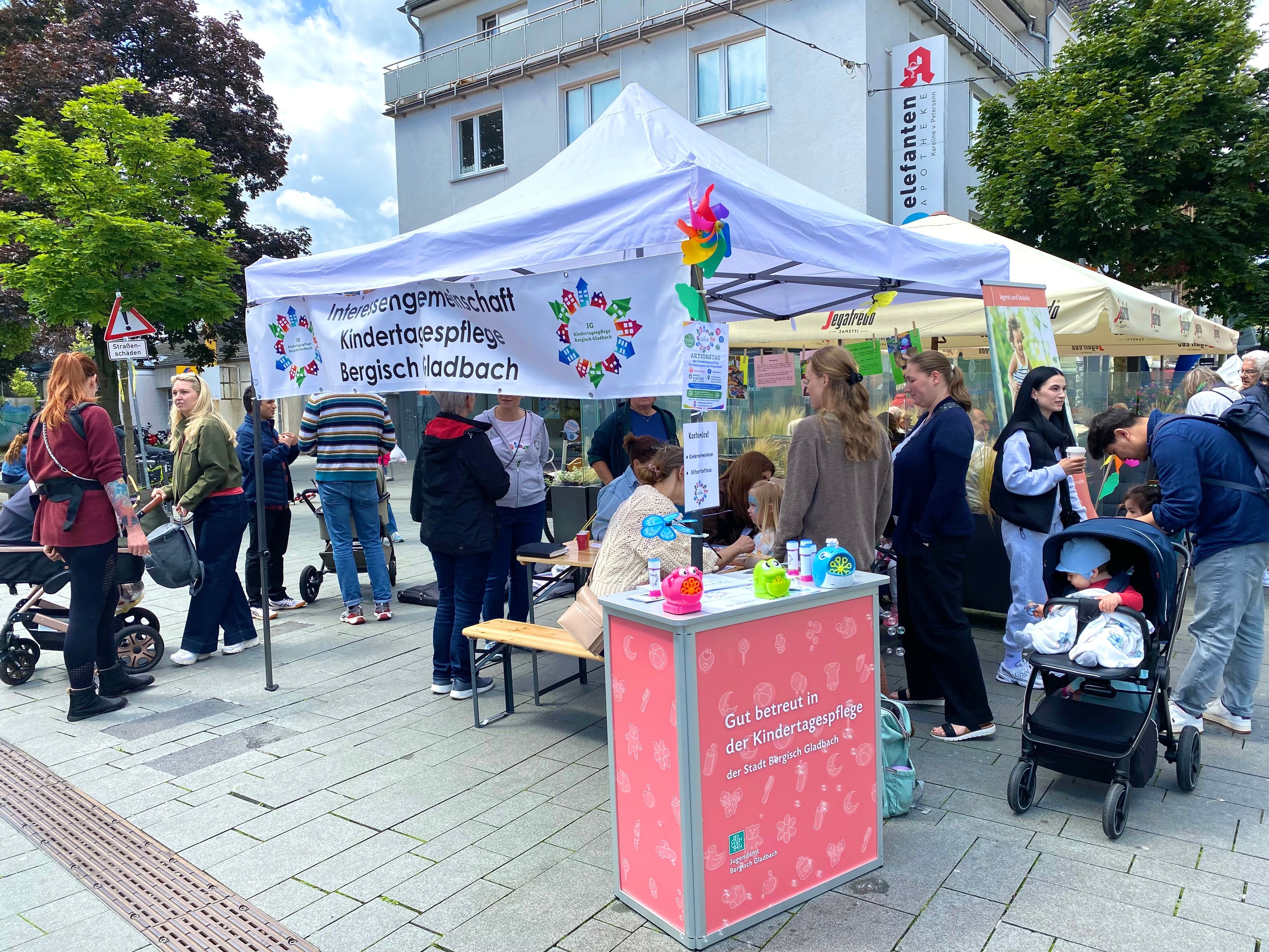 Um den Stand der Tagesmütter stehen viele Personen und unterhalten sich.