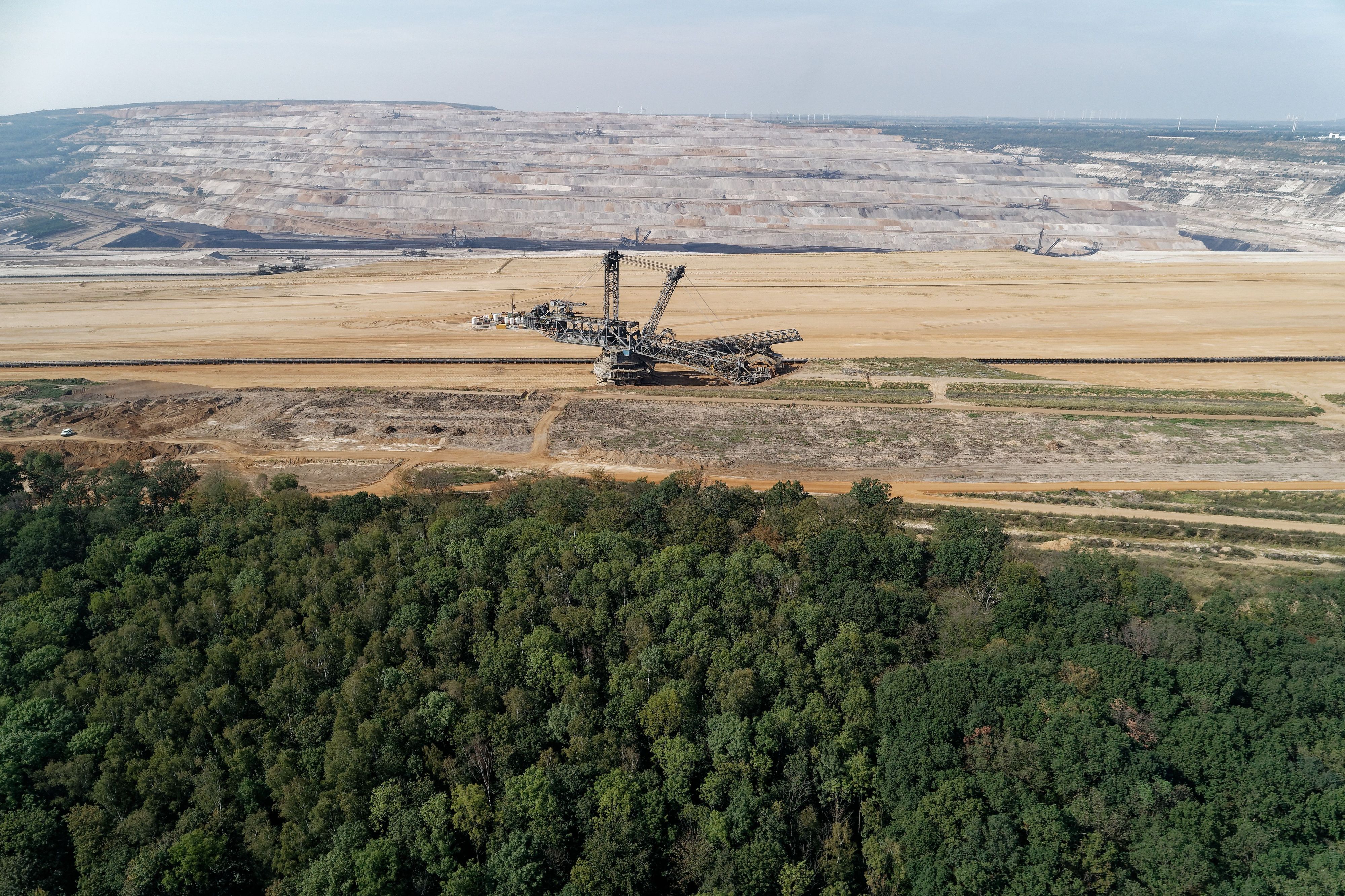 Das Foto zeigt den Tagebau Hambach mit einem Bagger, davor der Hambacher Forst.