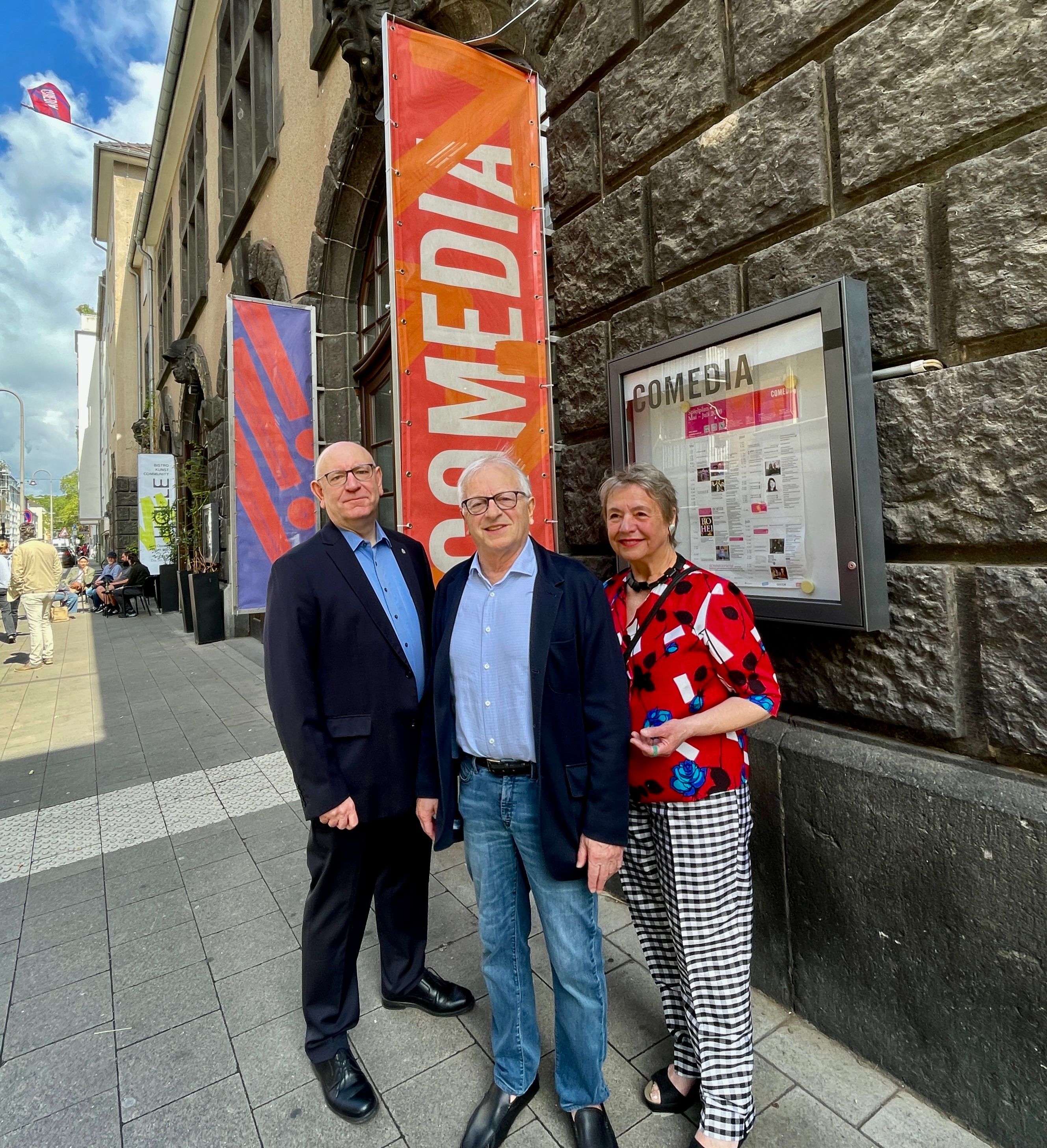 Zwei Männer und eine Frau stehen vor dem Gebäude der Comedia.