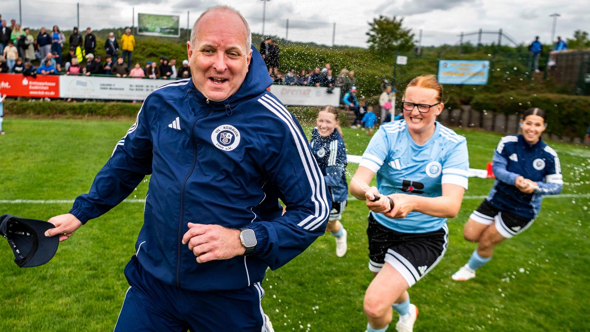 Der Trainer der siegreichen Mannschaft läuft vor seinen Spielerinnen davon, die ihn mit Bier duschen wollen.