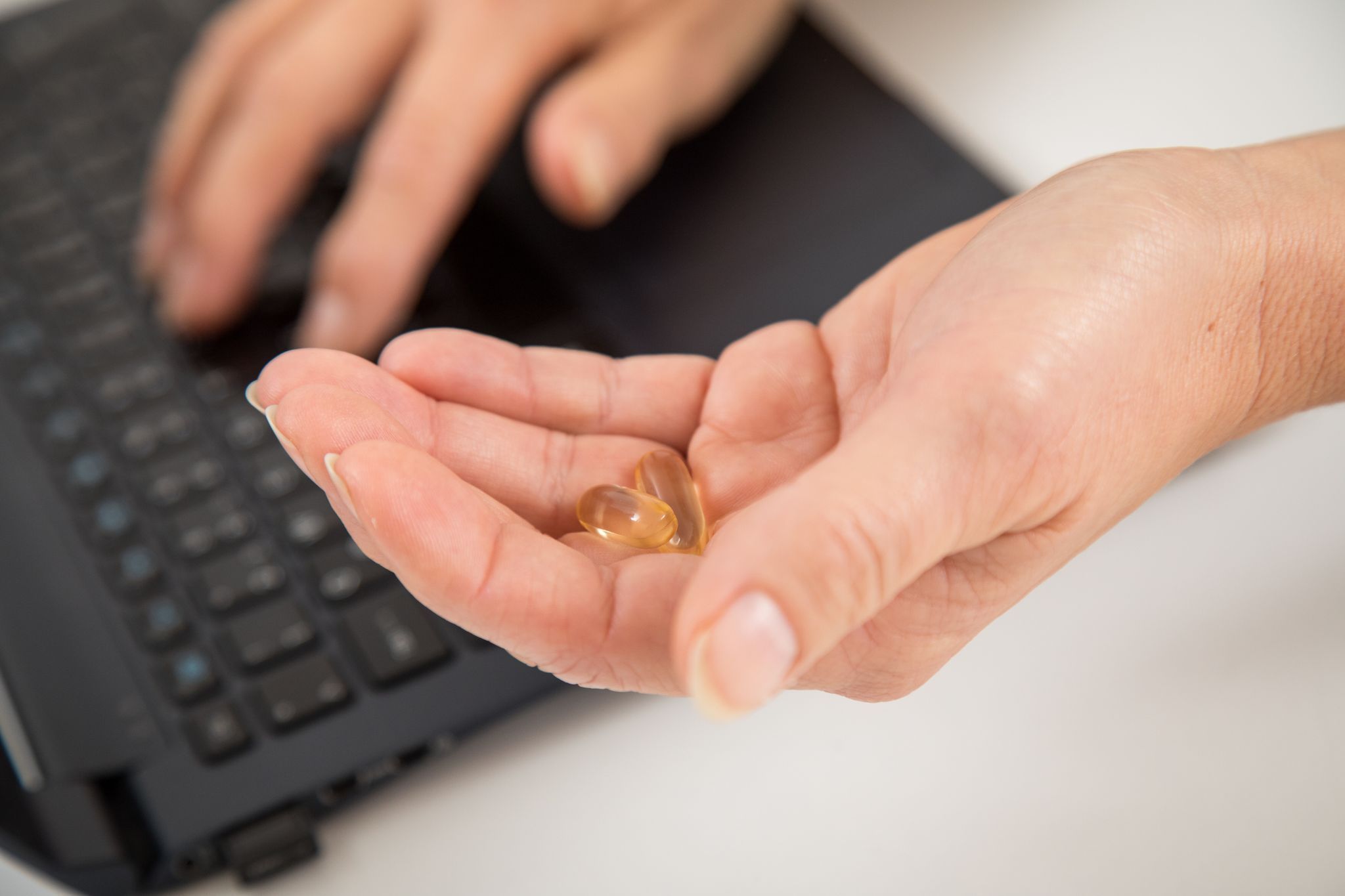Eine Frau sitzt am Laptop und hält Kapseln in der Hand