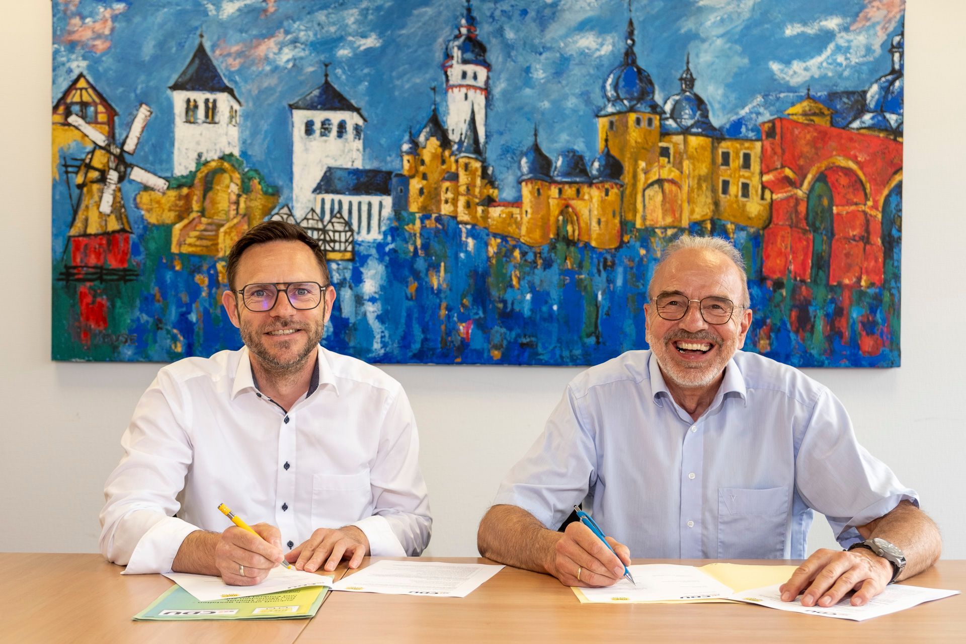 Björn Wassong und Dr. Manfred Rechs sitzen an einem Tisch und unterzeichnen eine Vereinbarung.