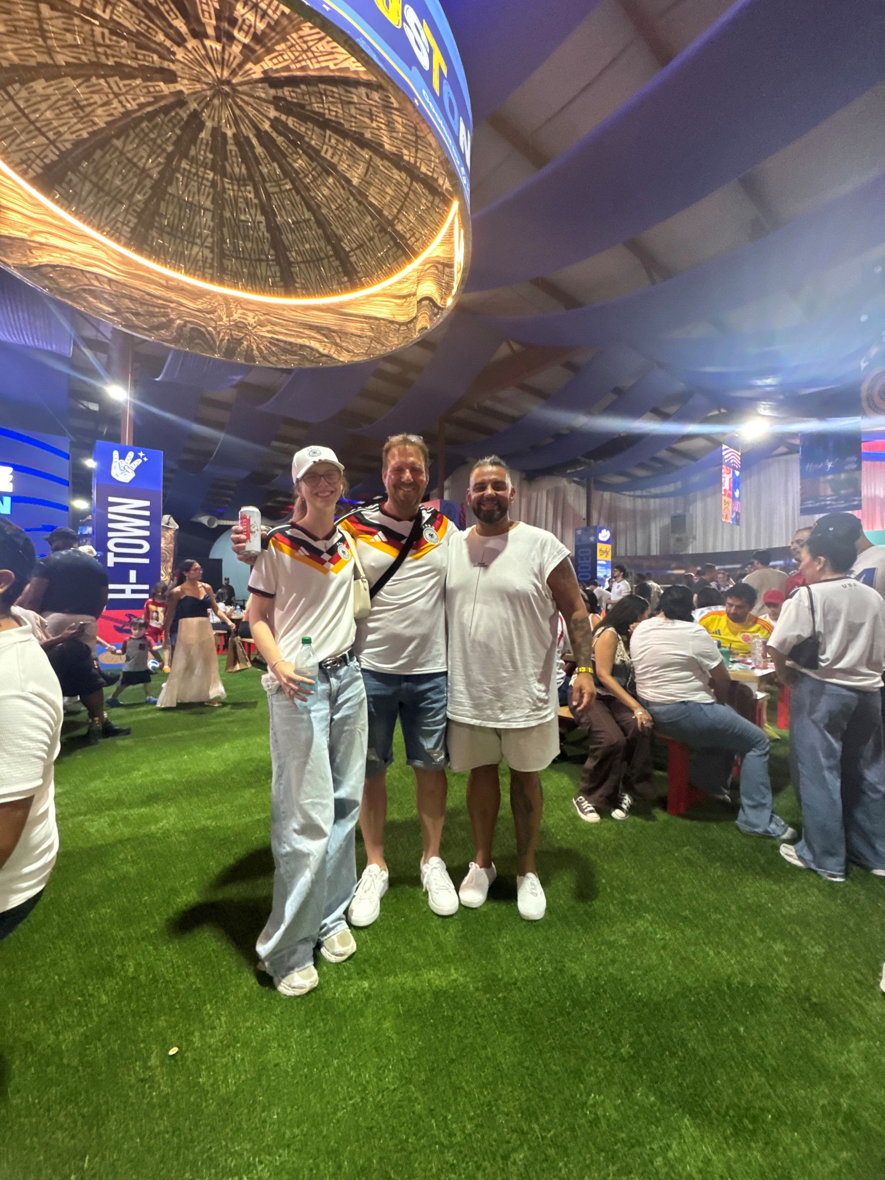 Marcello Volk steht neben zwei Deutschland-Fans im Trikot.