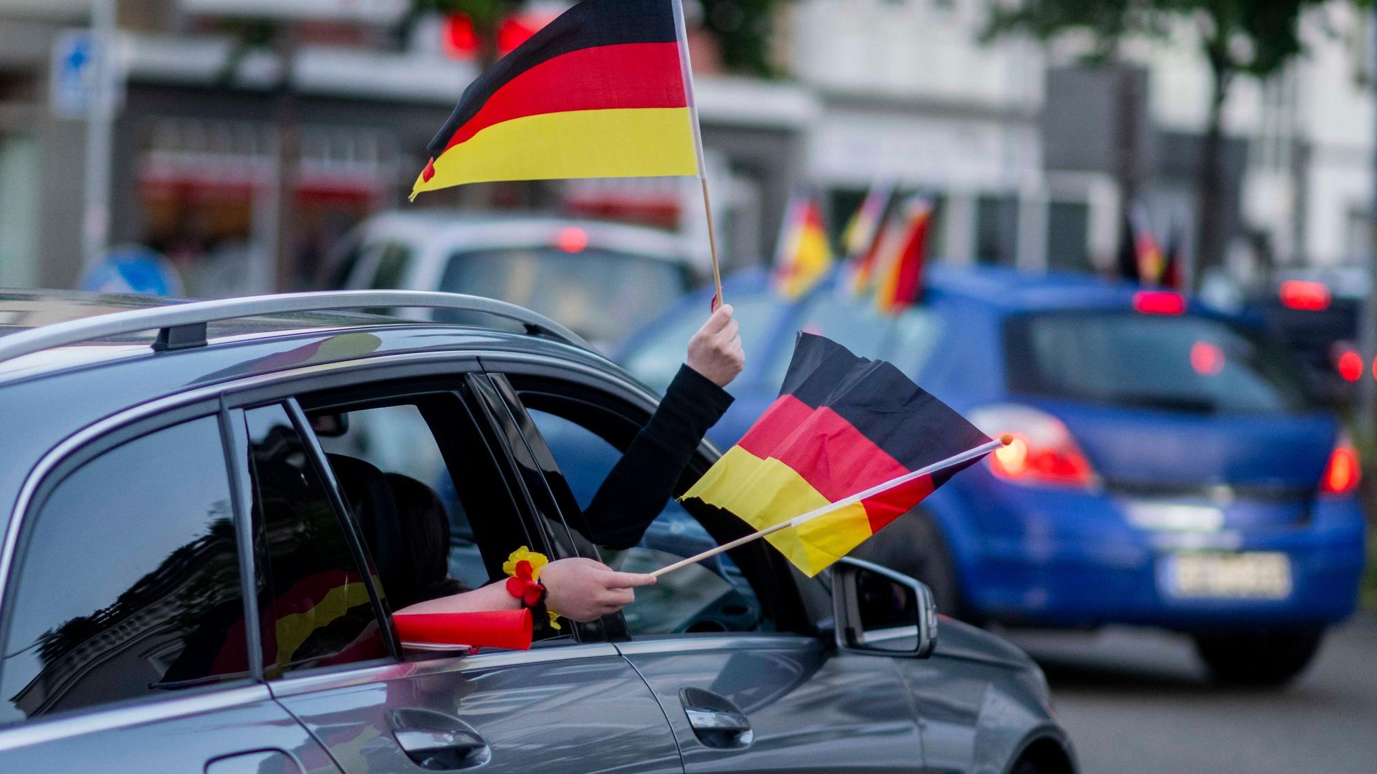 Aus einem Auto im Autokorso nach dem WM-Auftaktsieg wird mit zwei Deutschland-Fähnchen gewunken.