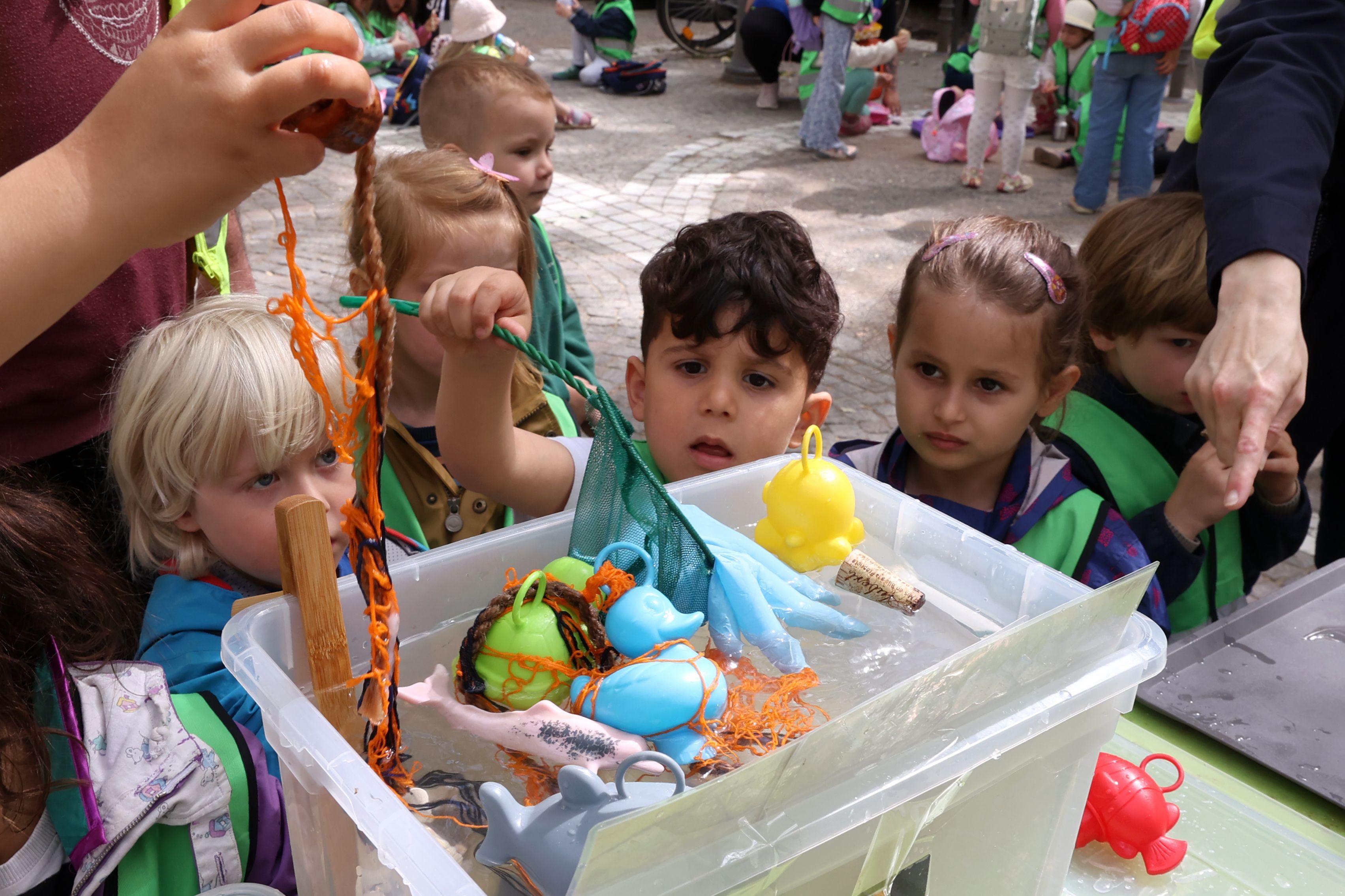 Kita-Kinder stehen vor einer Kiste mit Wasser, in der verschiedene Gegenstände schwimmen