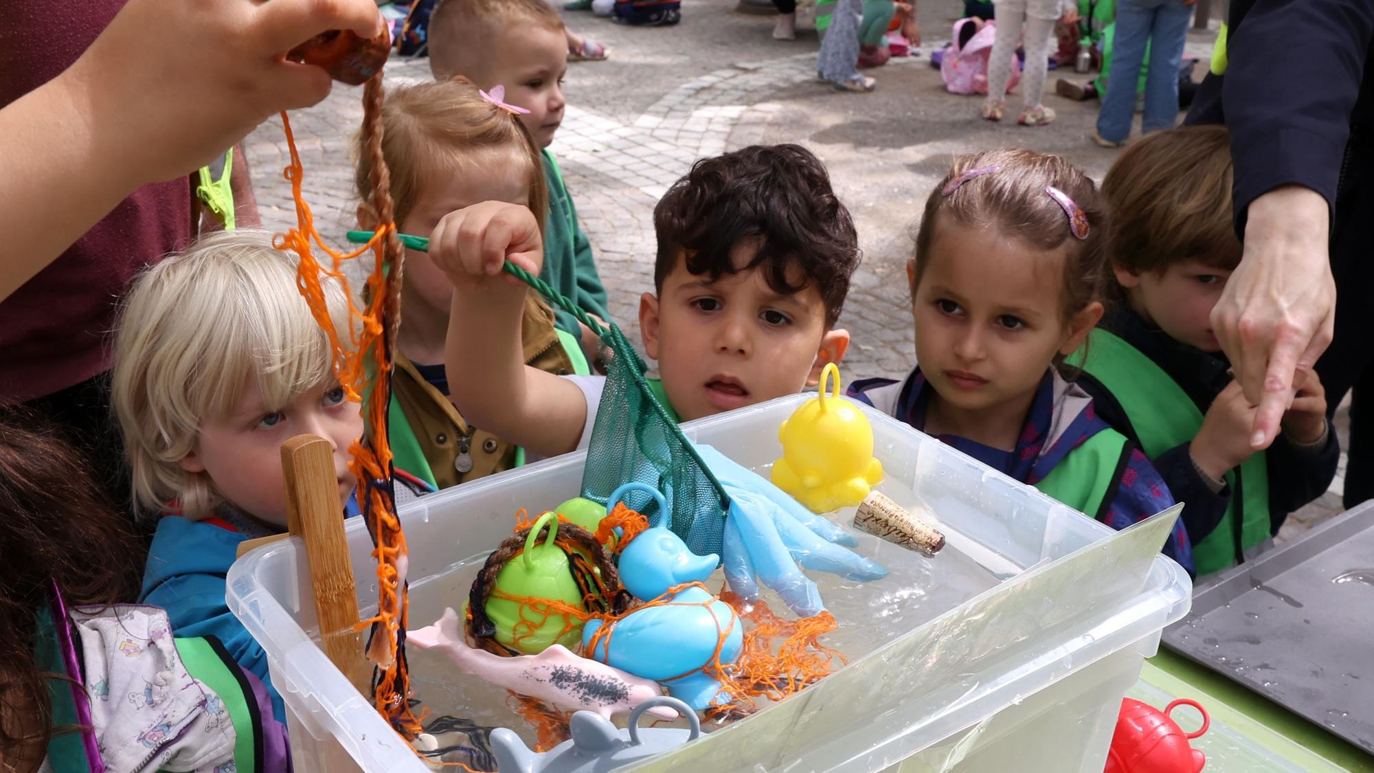 Kita-Kinder stehen vor einer Kiste mit Wasser, in der verschiedene Gegenstände schwimmen