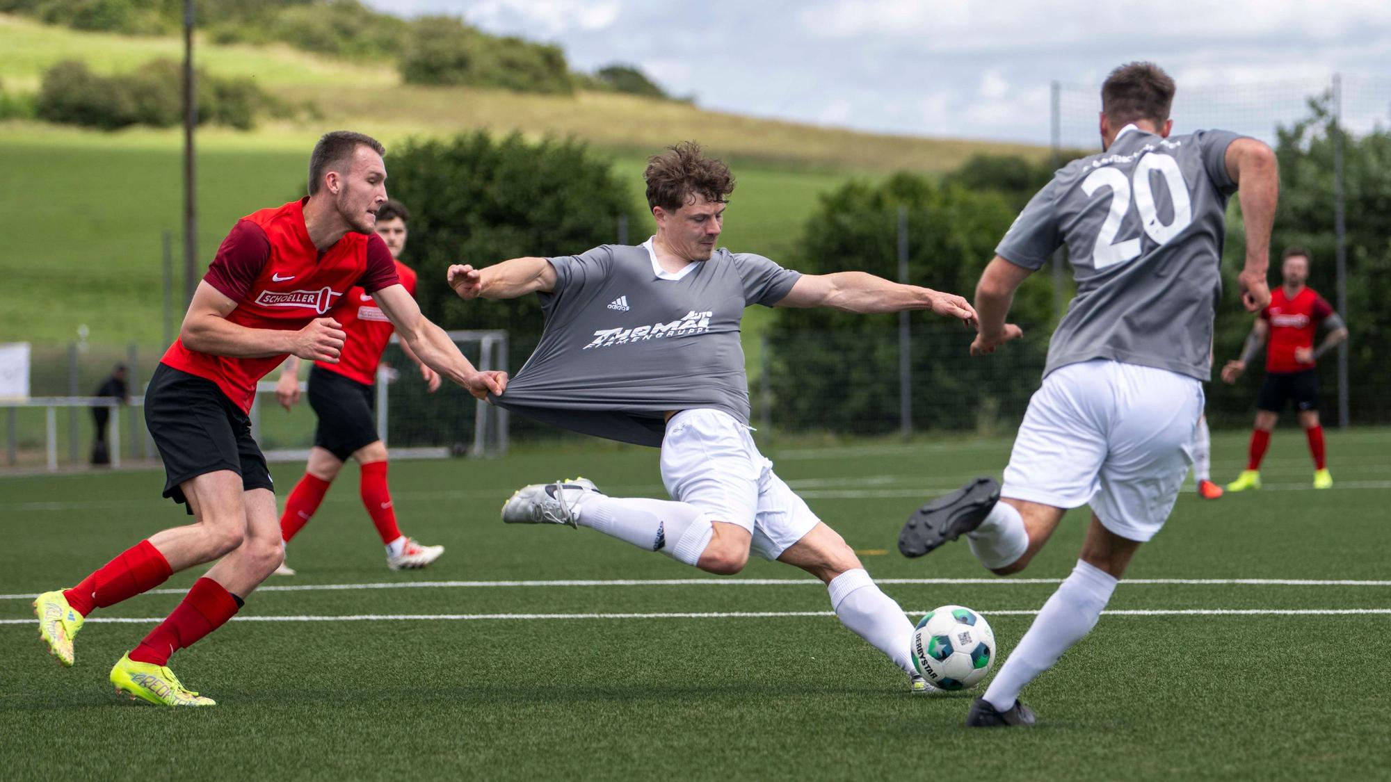 Ein Fußballer hält den ballführenden Gegenspieler am Trikot fest, das dadurch langgezogen wird.