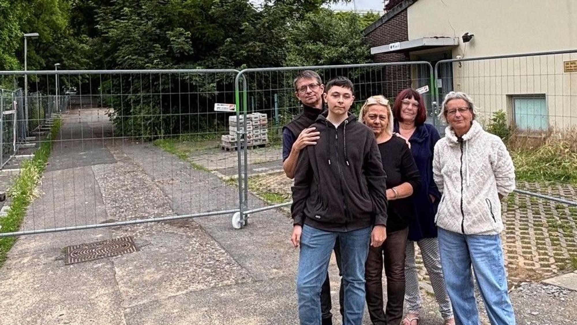 Auf dem Bild ist eine Gruppe von Nachbarn vor einem Bauzaun zu sehen.