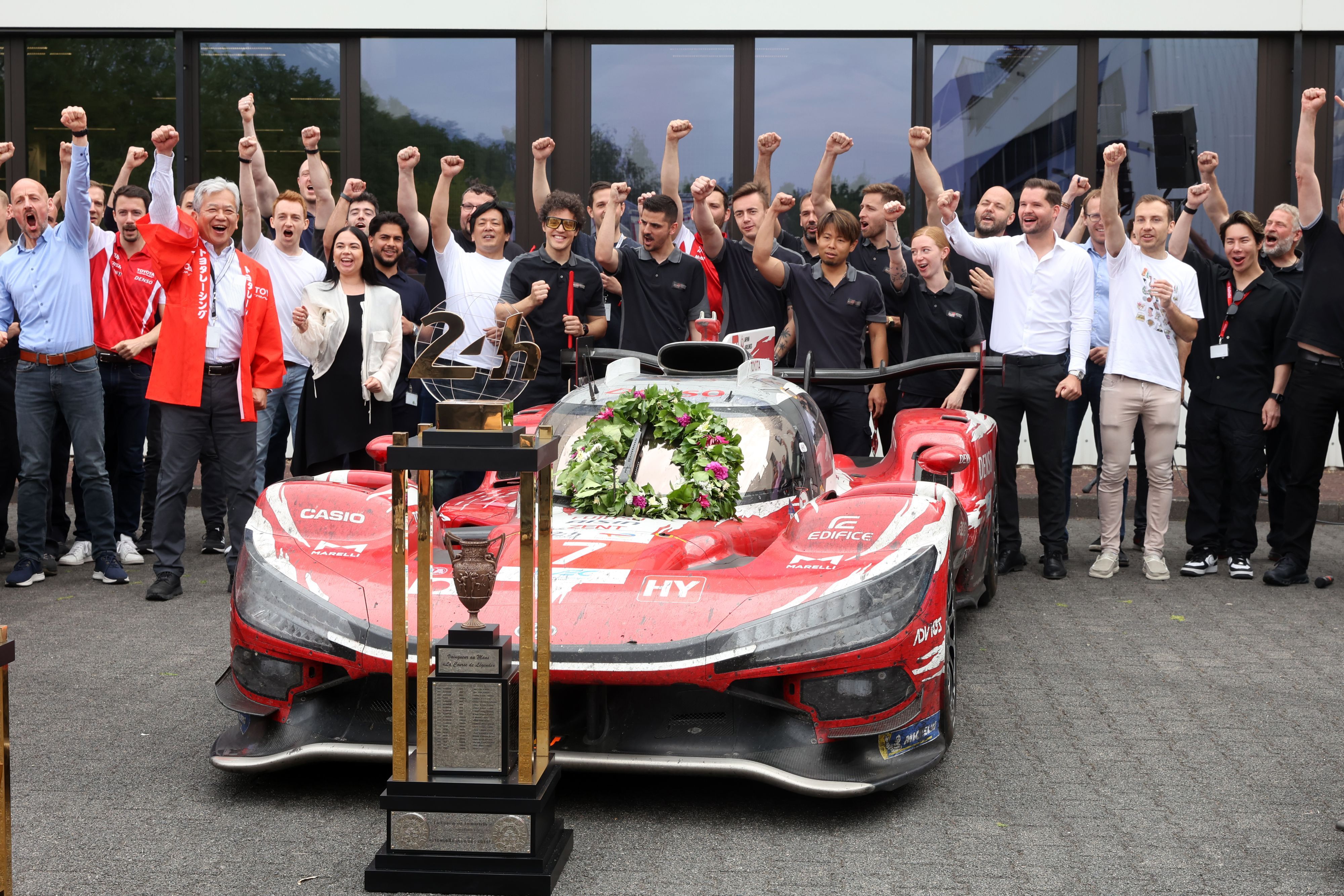 Mitarbeiter des Kölner Rennstalls Toyota Racing stehen hinter dem Siegerfahrzeug des Autorennens „24 Stunden von Le Mans“ und jubeln.